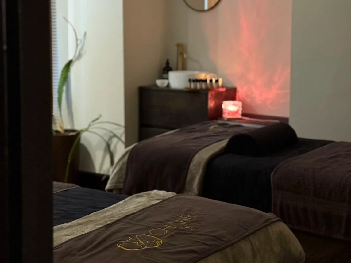 A dimly lit room with two massage beds, each covered with brown blankets.