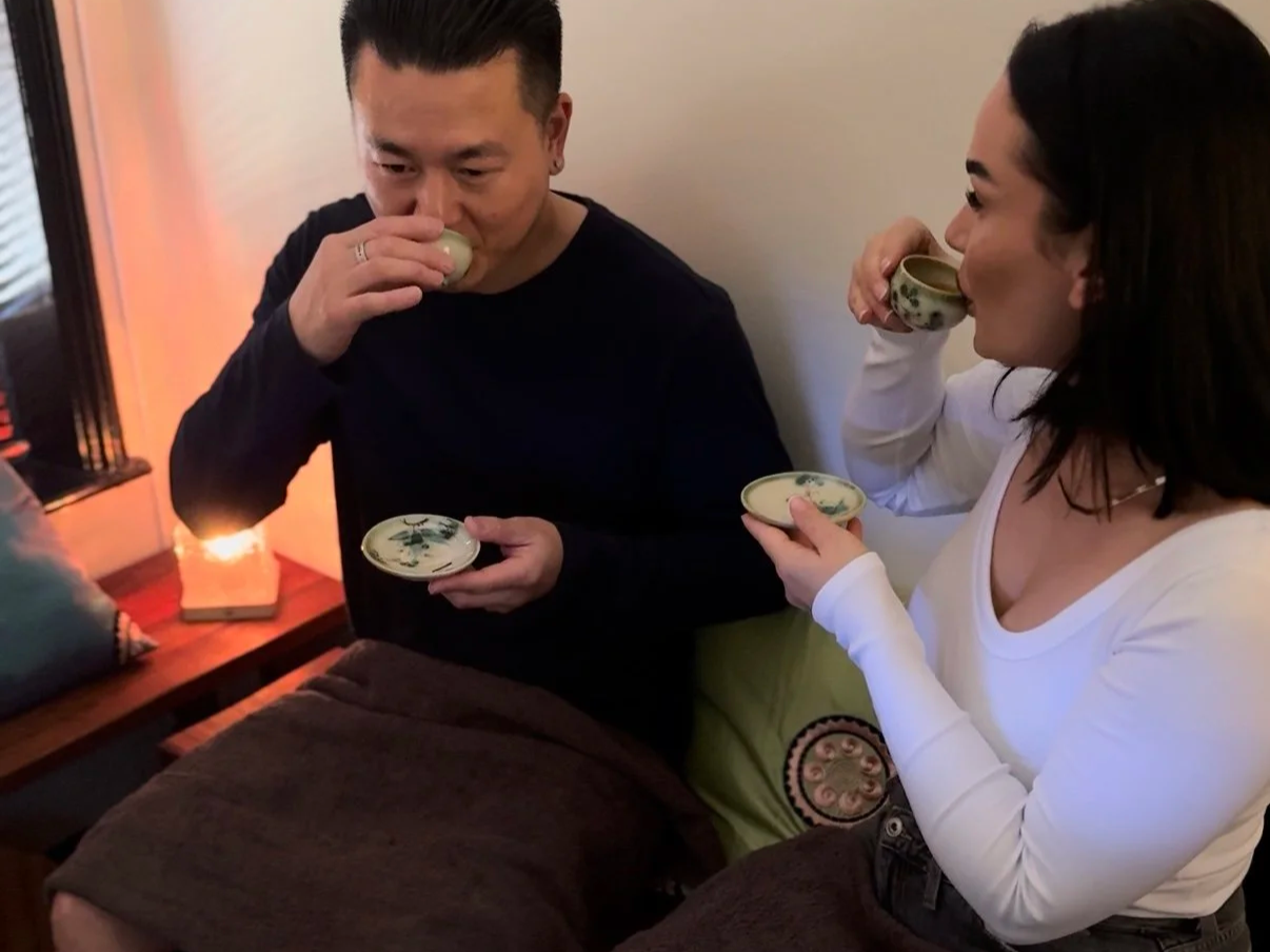 Two people drinking tea or sake from small cups in a cozy room.
