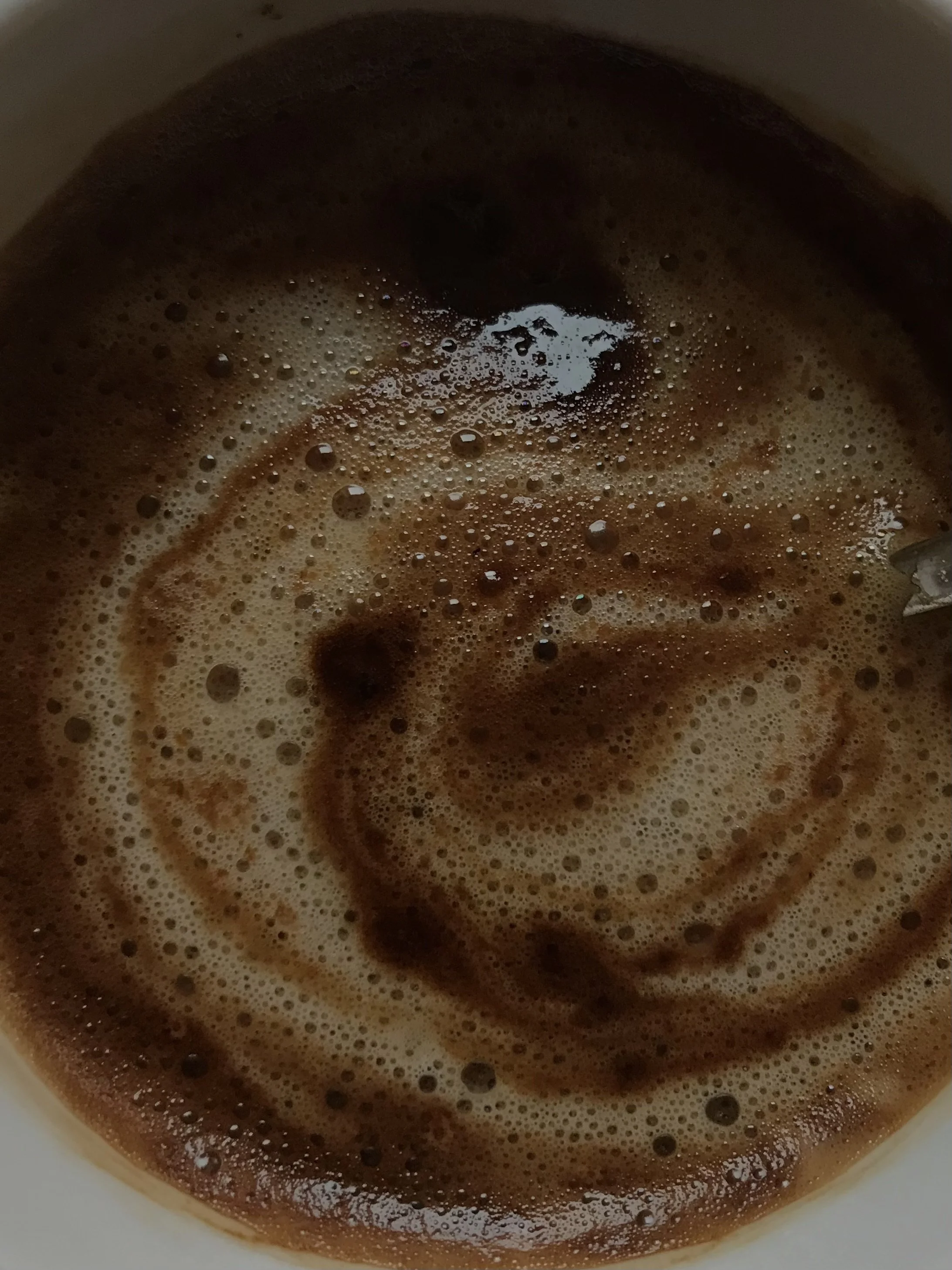 A close-up view of a cup of hot chocolate with foam and a cinnamon stick.