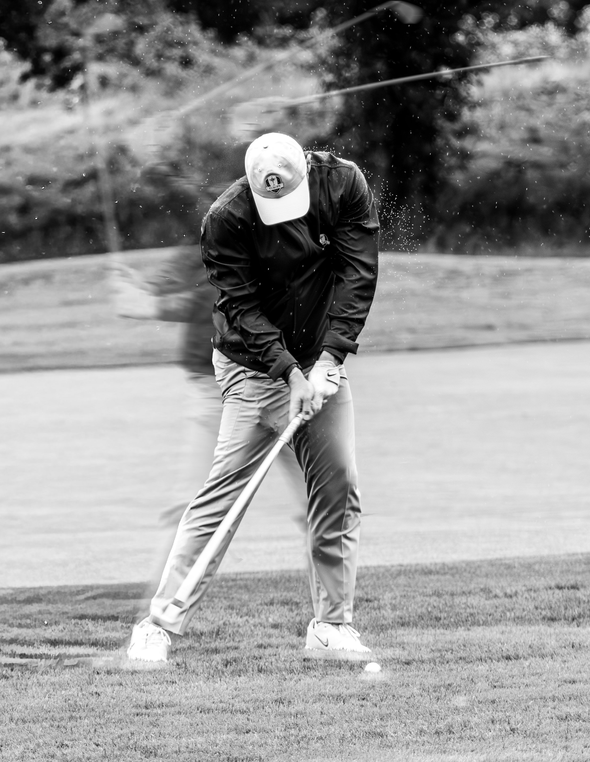 Rory McIlroy playing golf, preparing to hit a golf ball on a golf course, wearing a cap, jacket, and pants at the Ryder Cup.