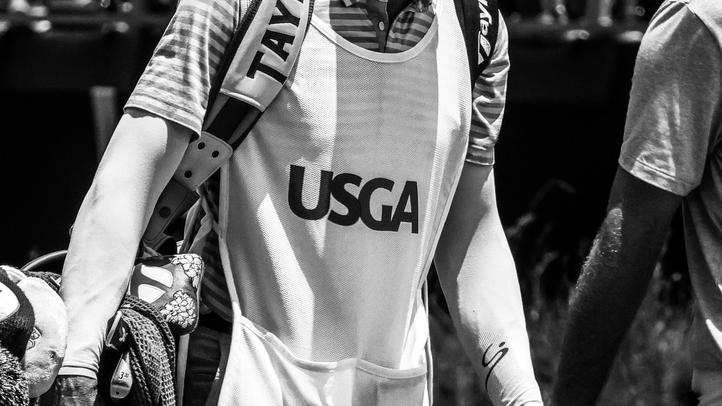 Close-up of a person wearing a USGA apron, with a golf glove in hand, possibly at a golf course or event, in black and white.