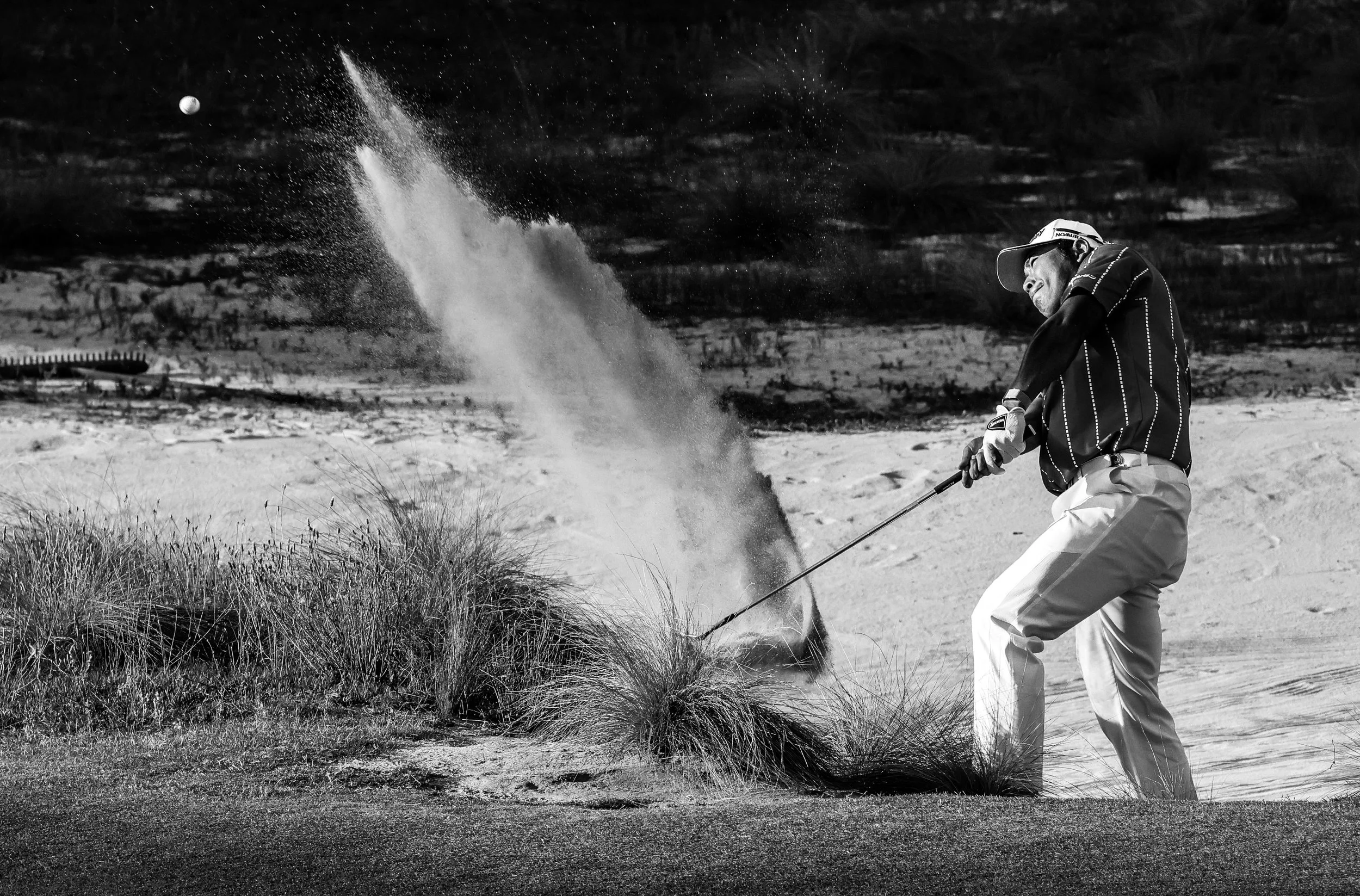 A person playing golf sand scraping on a sand trap or bunker during daytime in sandy, grassy terrain.