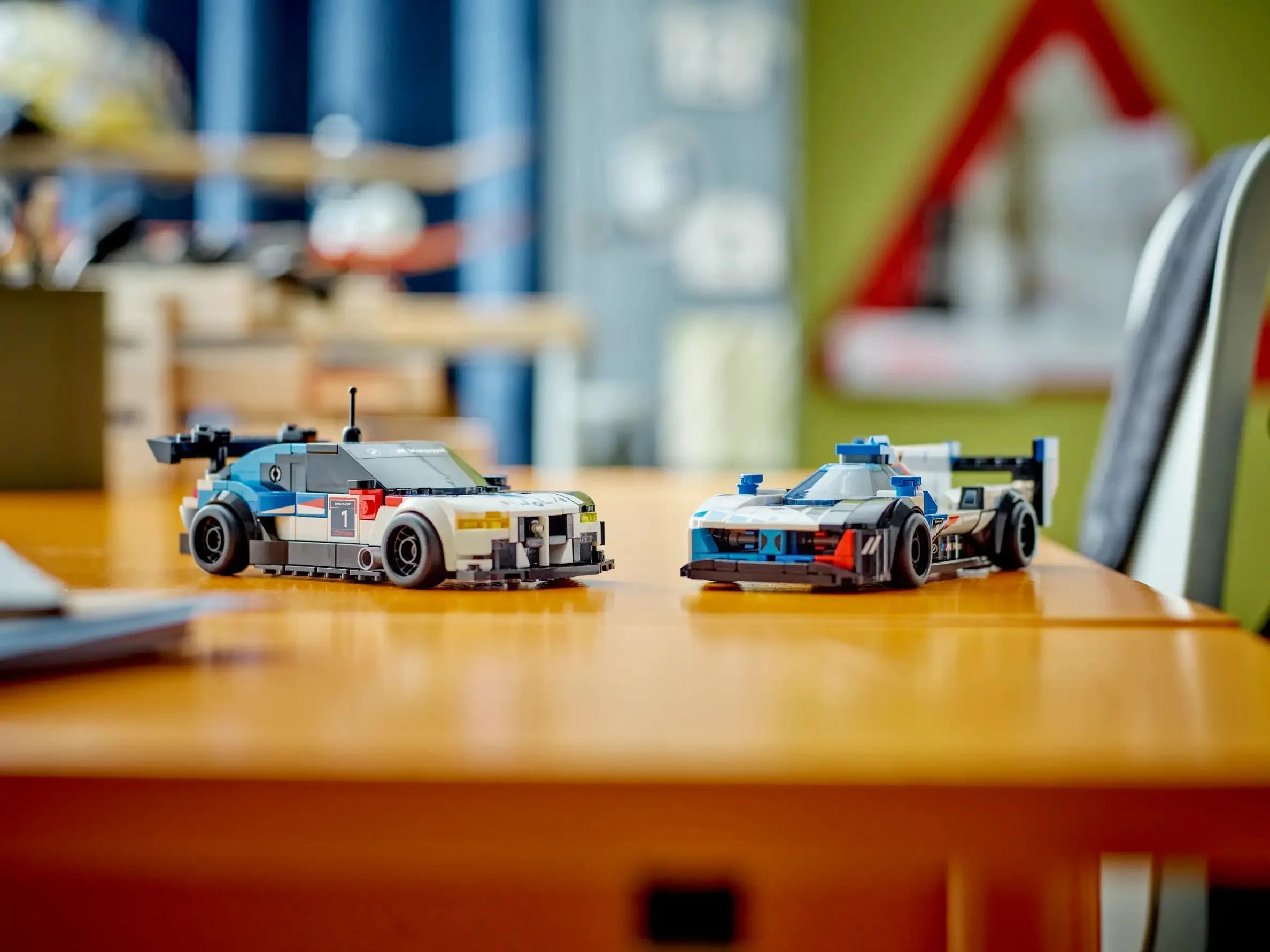 Two LEGO race cars on a wooden table in a room with colorful decorations and furniture.