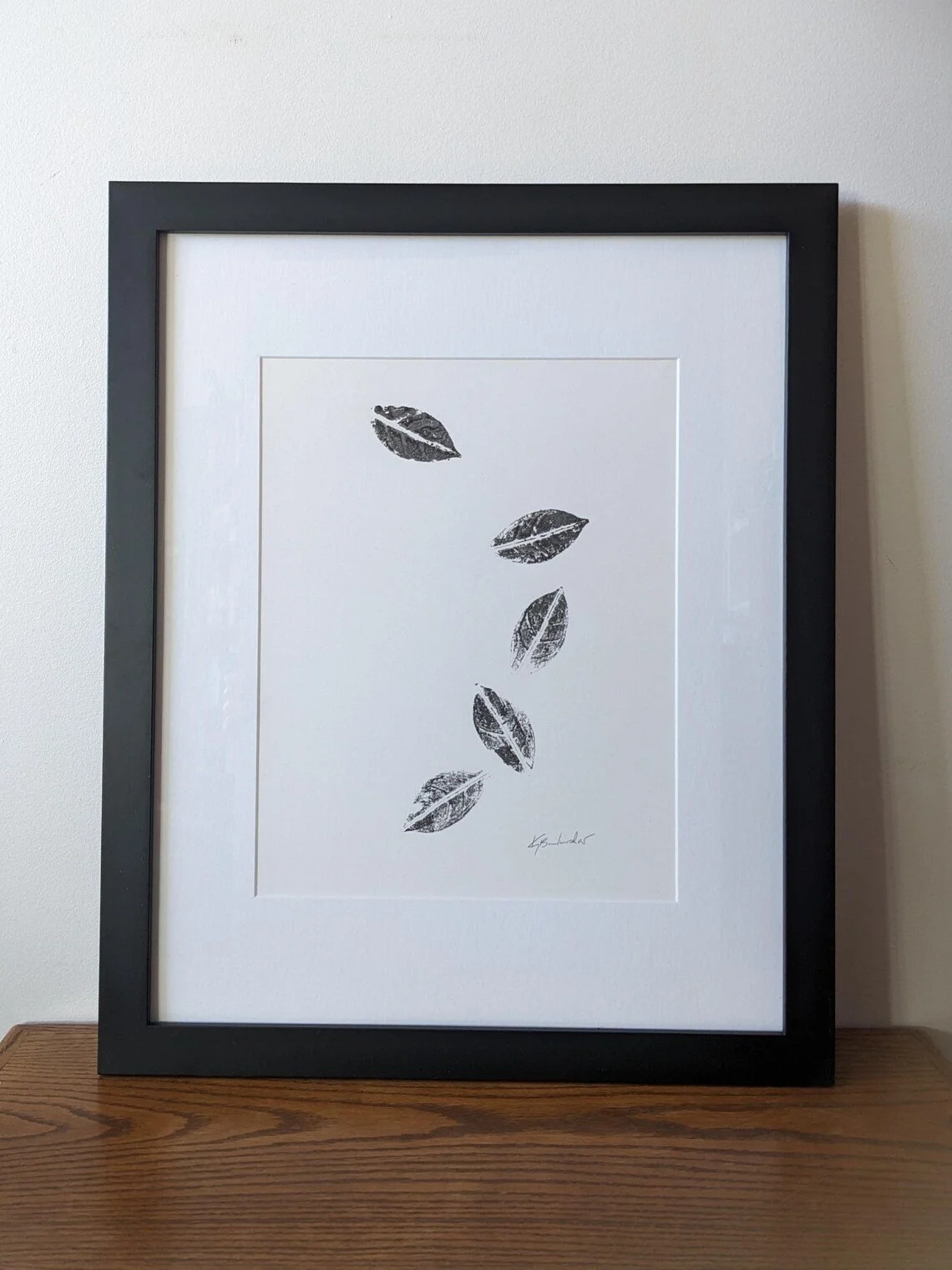 Framed artwork of six black and white leaf prints arranged vertically on white background