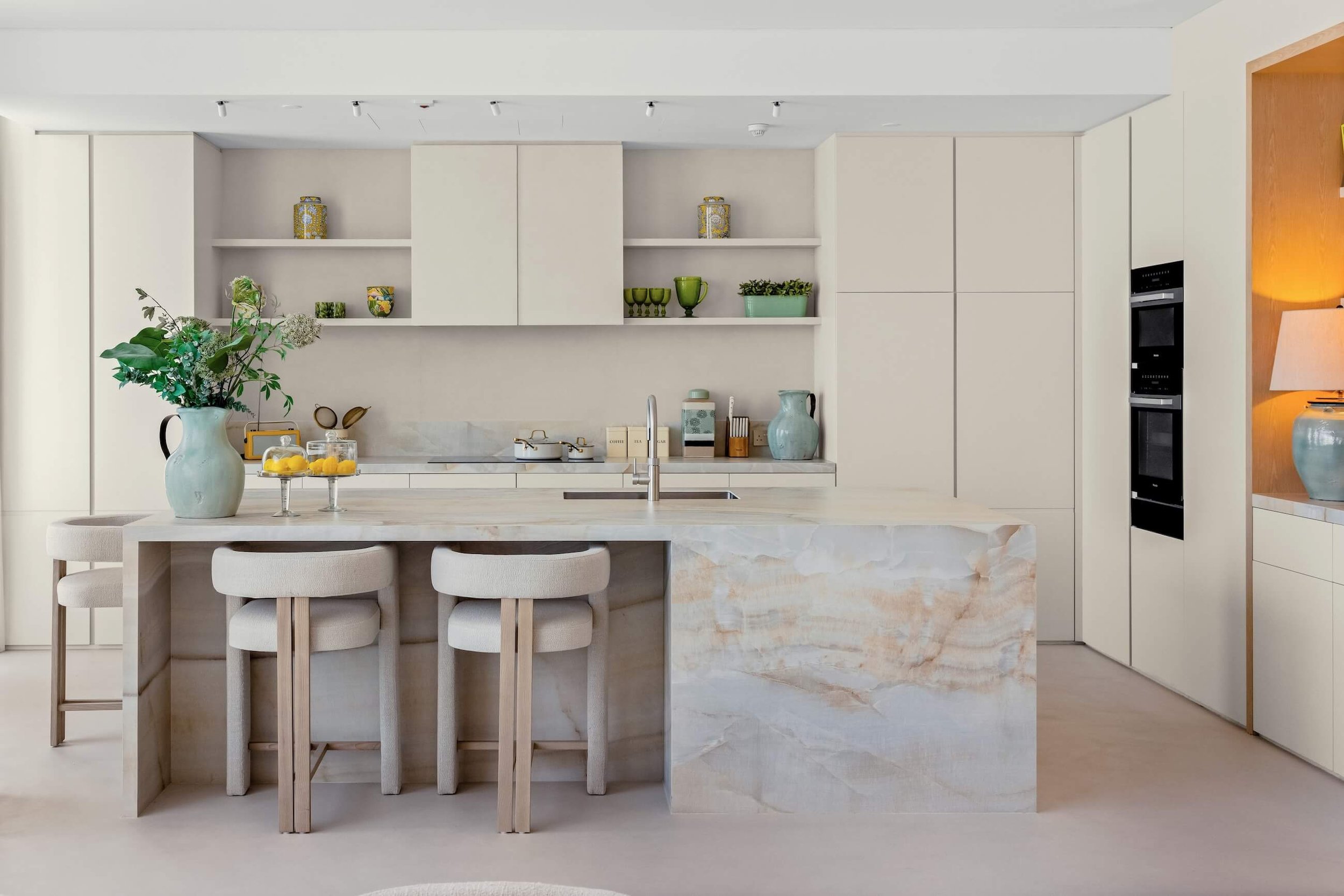 Modern minimalist kitchen with off-white cabinetry and a marble island counter with a vase of green and white flowers.