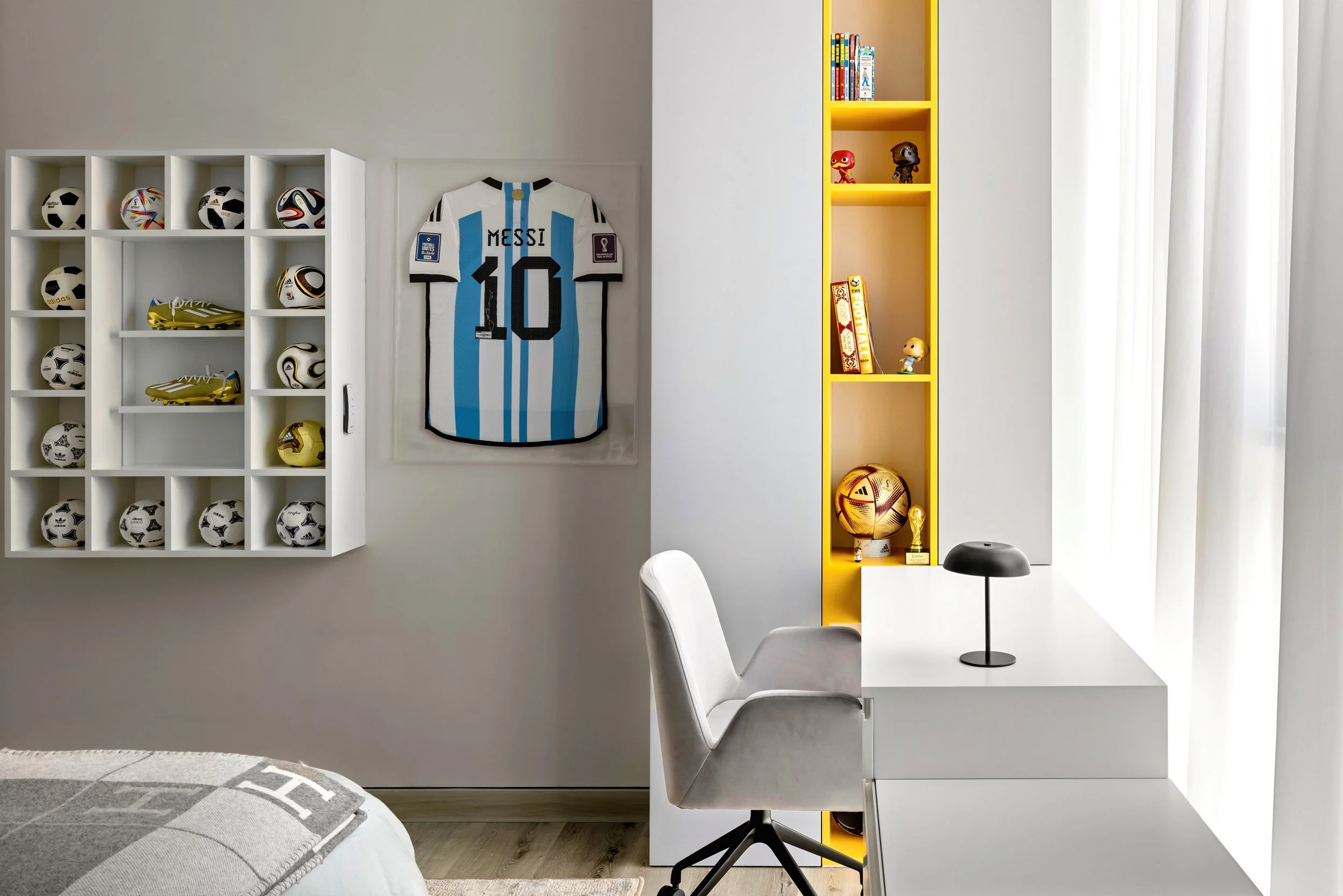 Dubai kids’ bedroom with wall-mounted shelving for football collectibles, illuminated vertical storage, and a clean white study desk. Interior photography by Kamie Spaces.