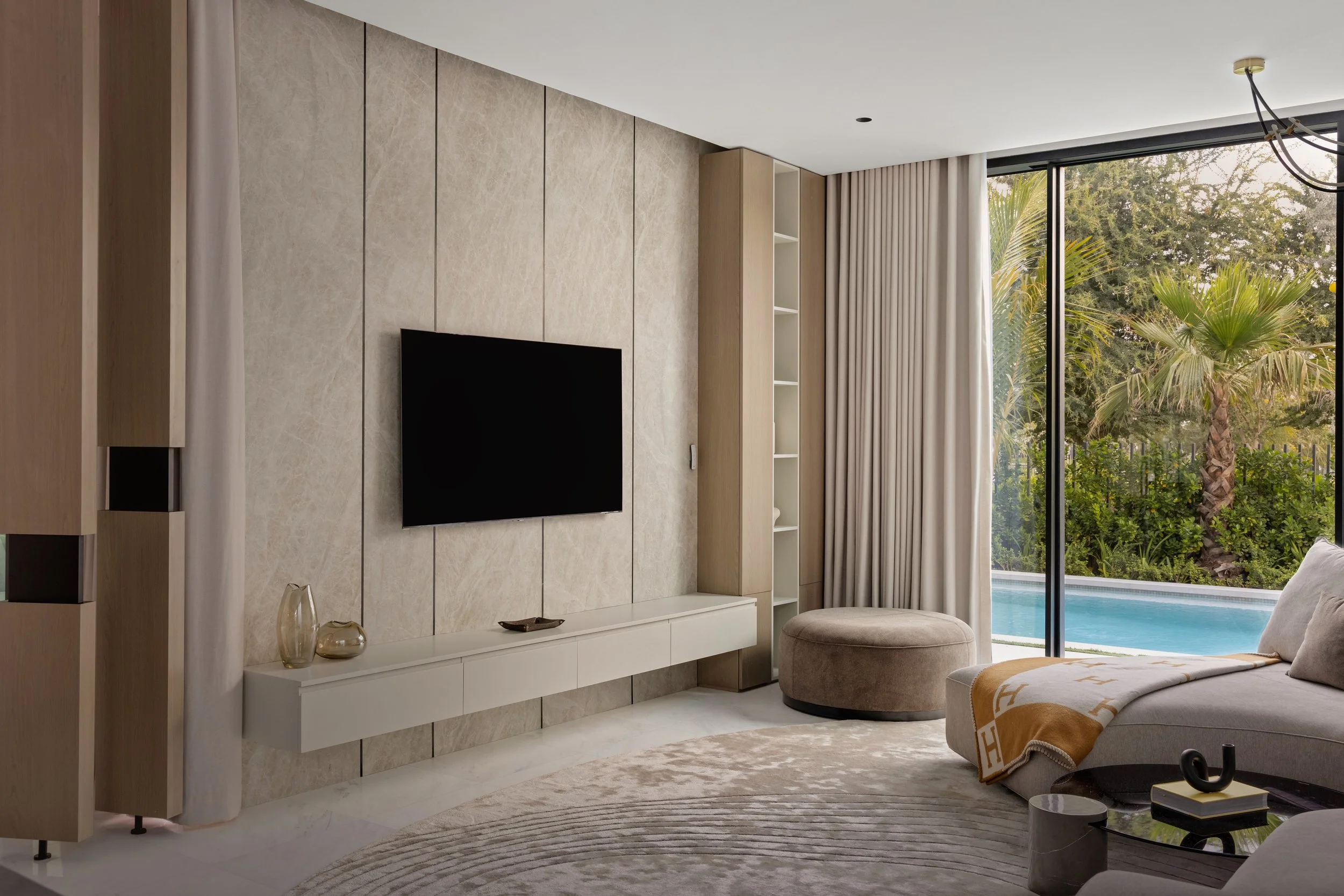 Modern living room interior with soft natural light, textured wall panels, and pool view. 