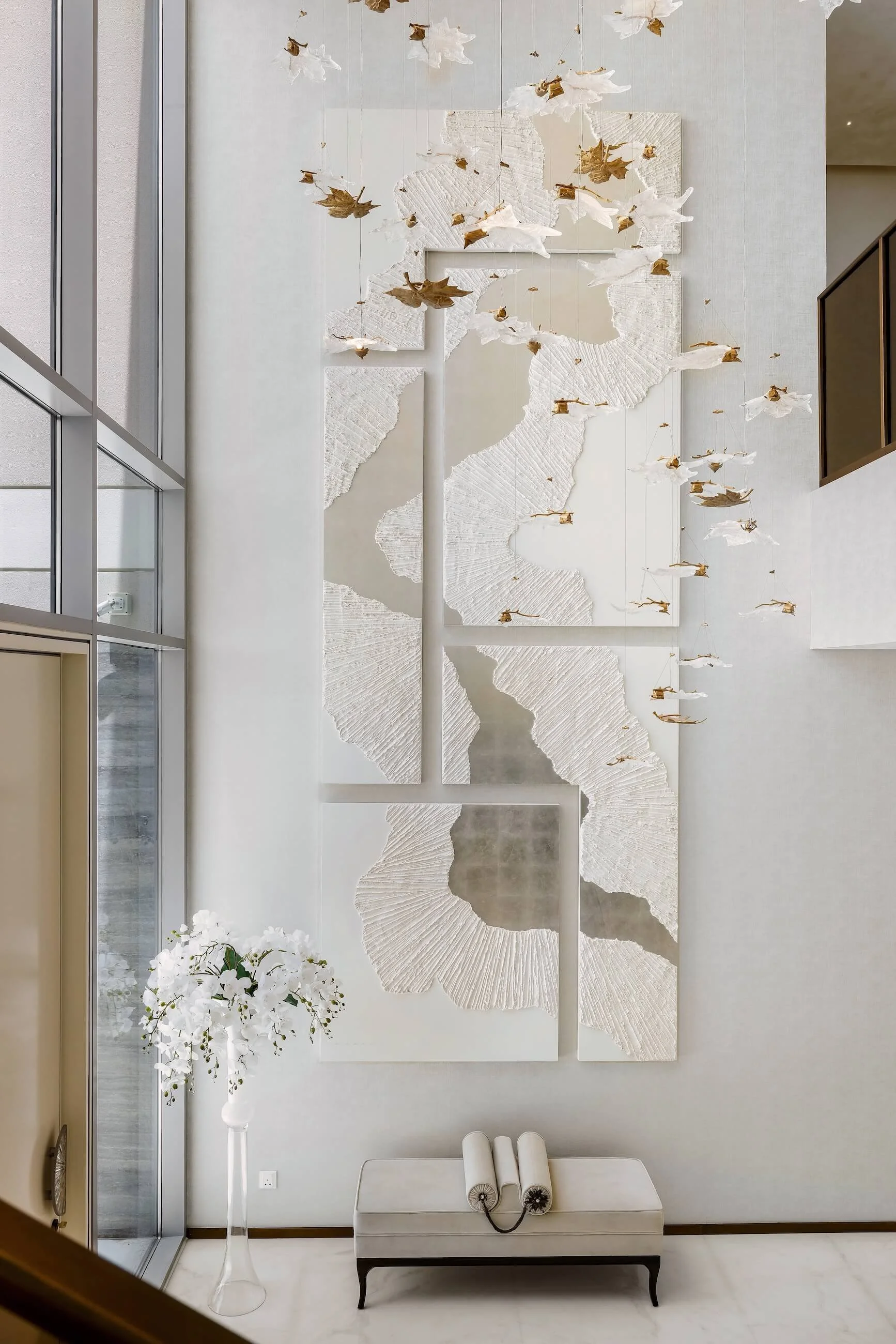Modern interior wall decor with textured white panels and an art installation of hanging white and gold paper birds.