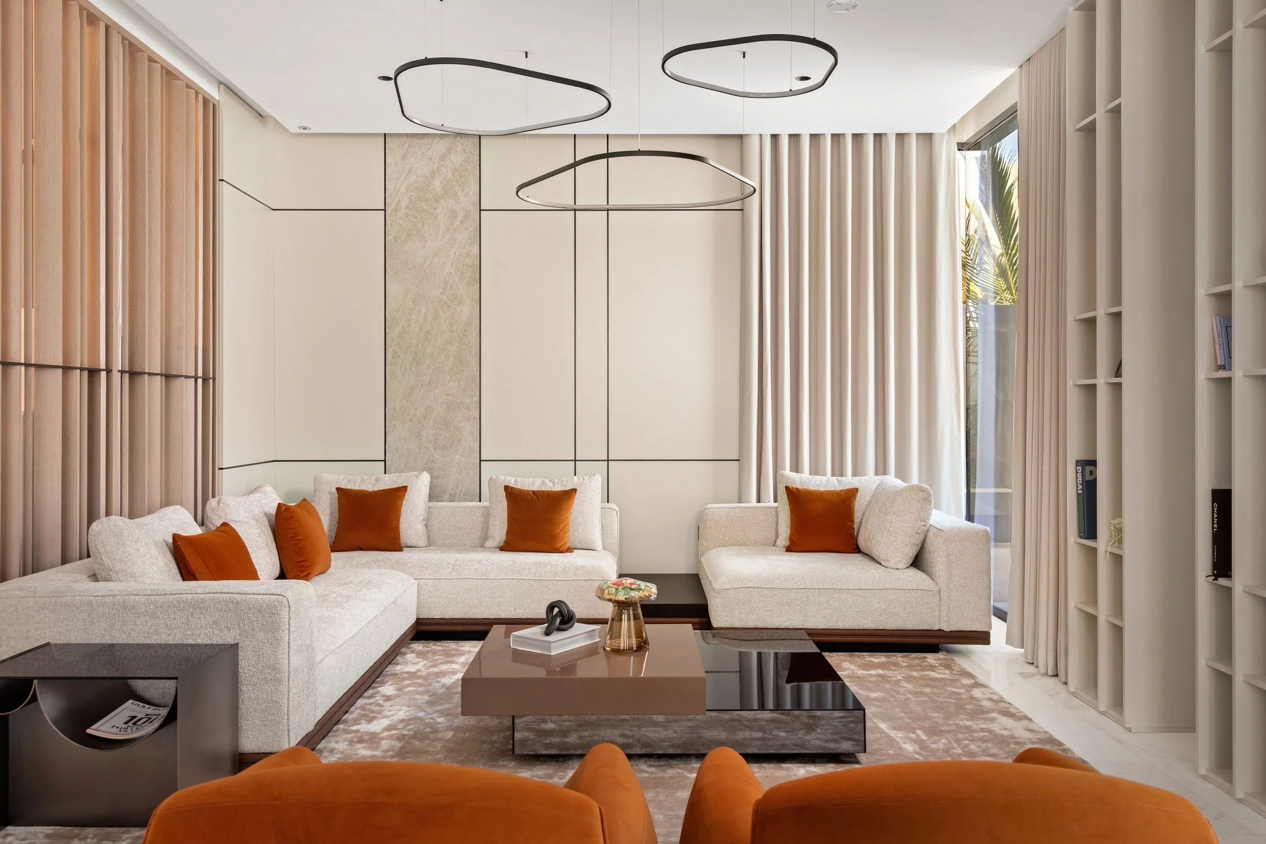 Dubai villa living room with custom panelled walls, cream sofas, orange cushions, and modern ceiling lights. Interior photography by Kamie Spaces.