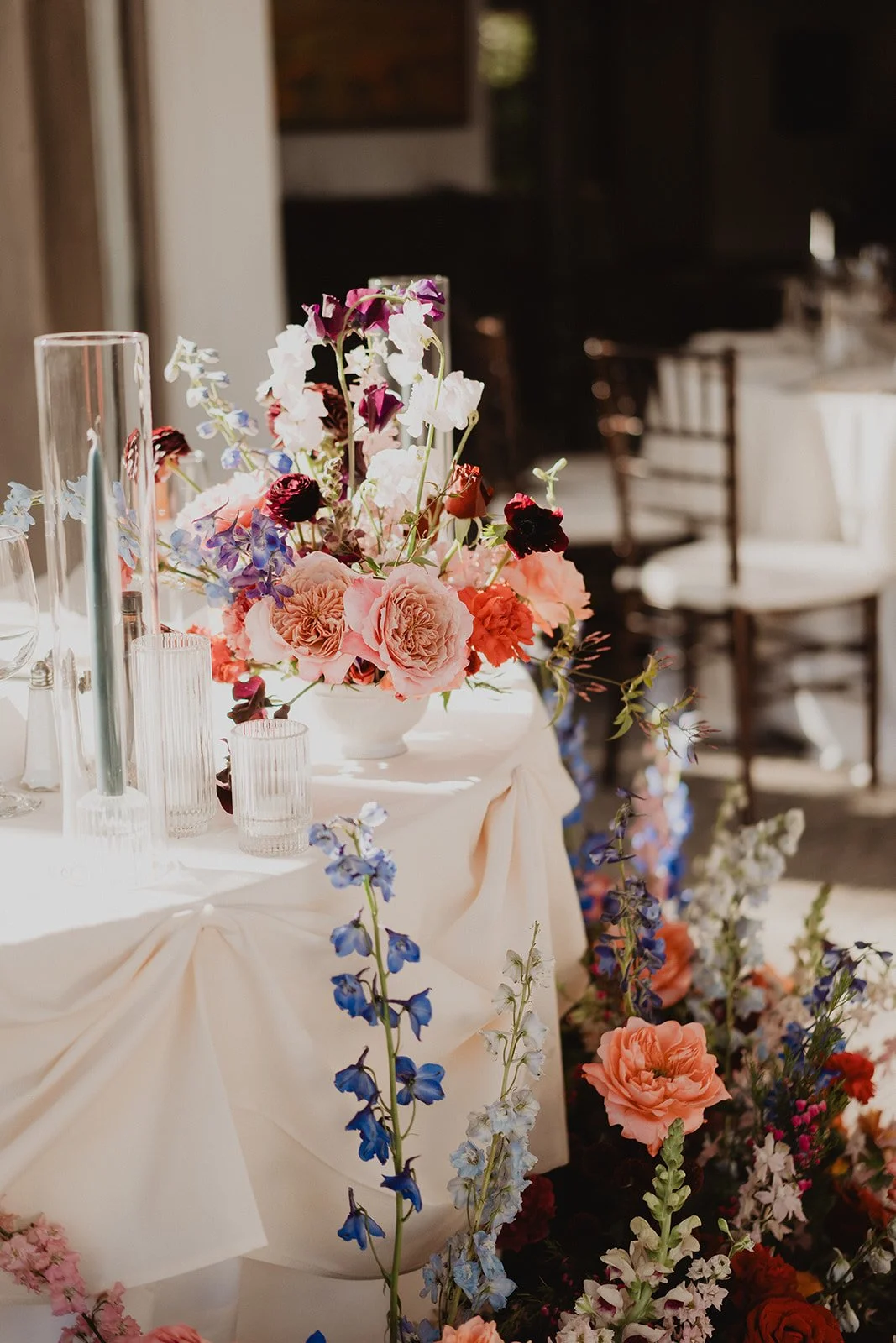 Elegant floral arrangement on a table with pink, purple, and blue flowers, and some candles, set for a celebration or event.