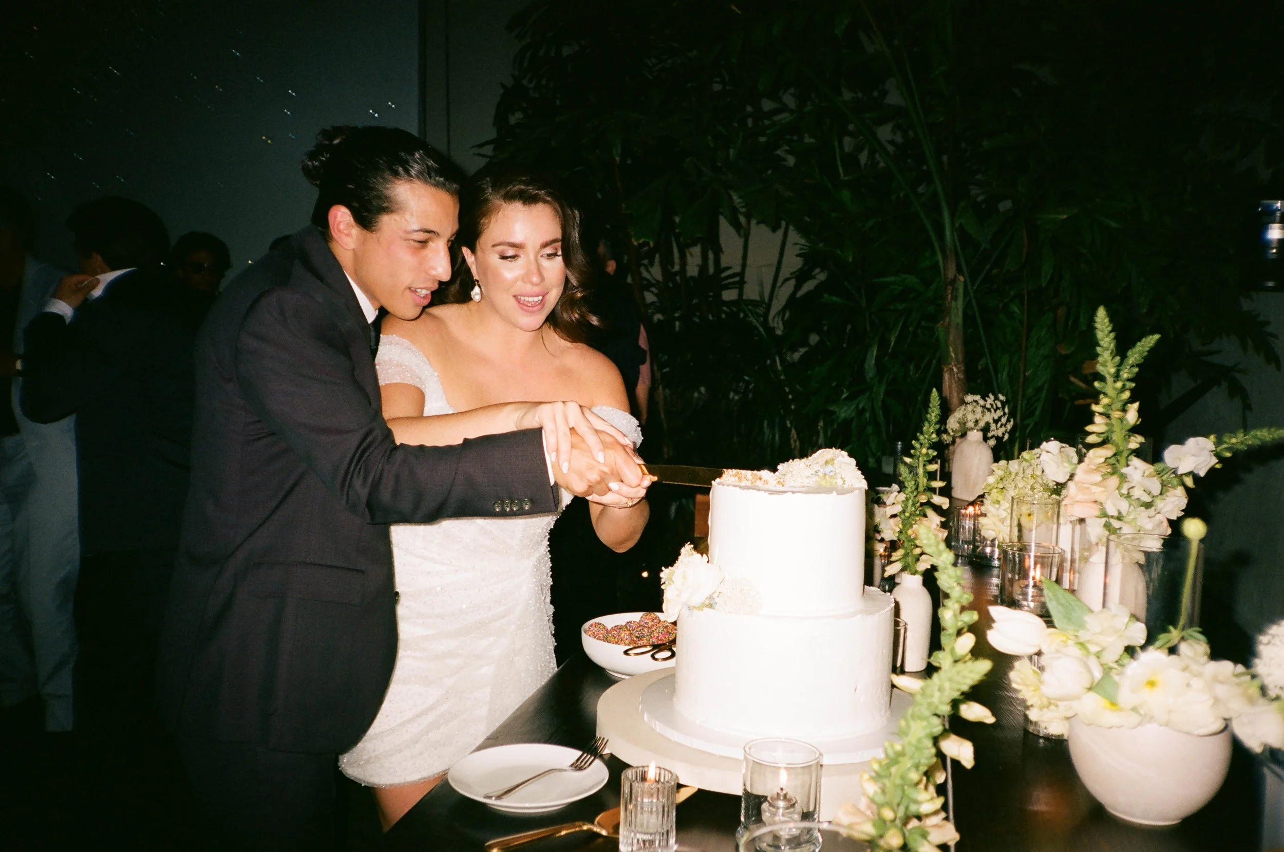 A man and woman in formal attire cutting a wedding cake at a celebration event, surrounded by flowers and decorations.
Carolyn + Ben Wedding, Millwick DTLA