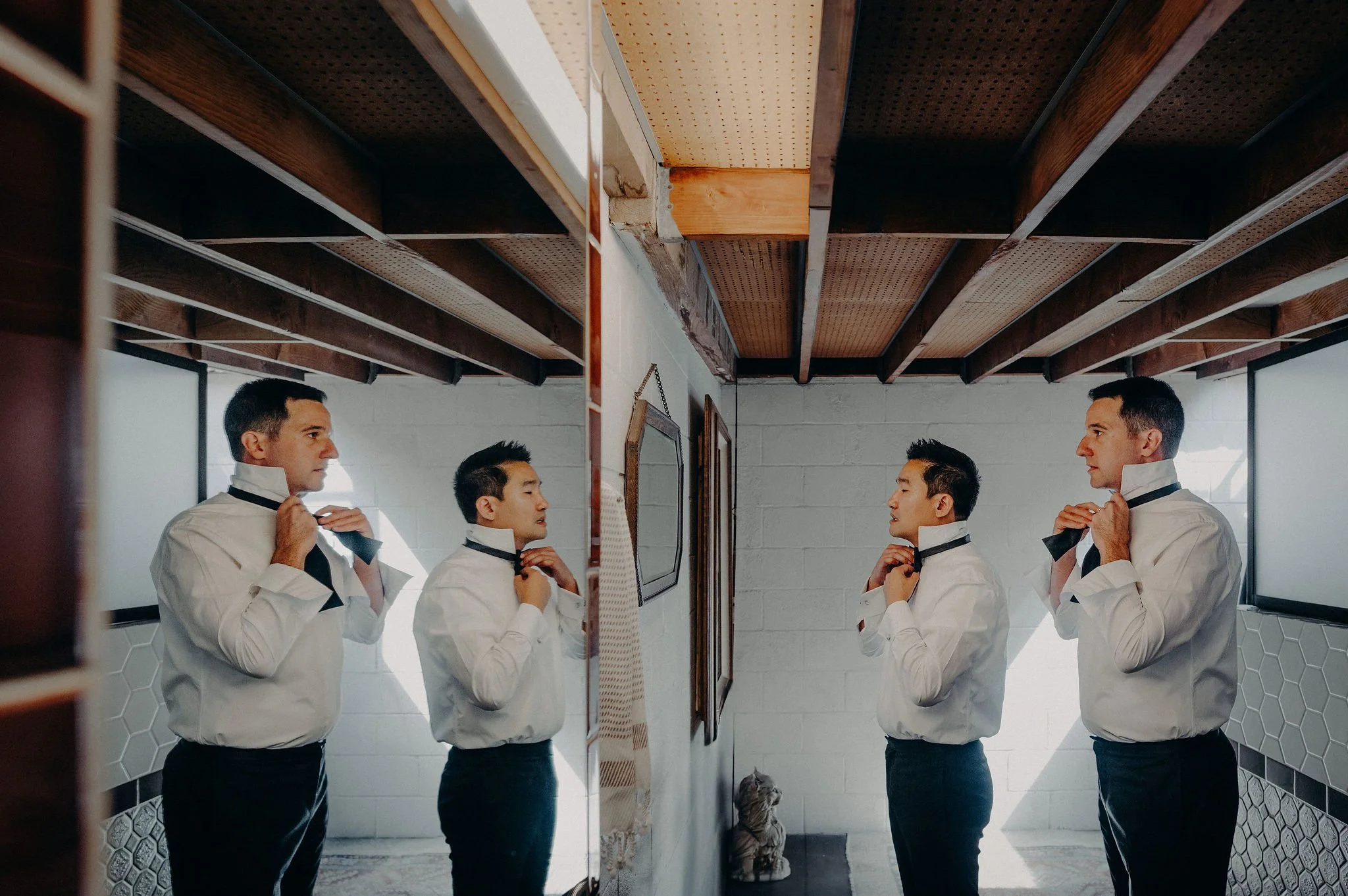 Six men in white shirts and black ties adjusting their collars in front of mirrors in a bathroom with white tiled walls and a wooden ceiling.
Cliff + Warren wedding. Smog Shoppe, Culver City