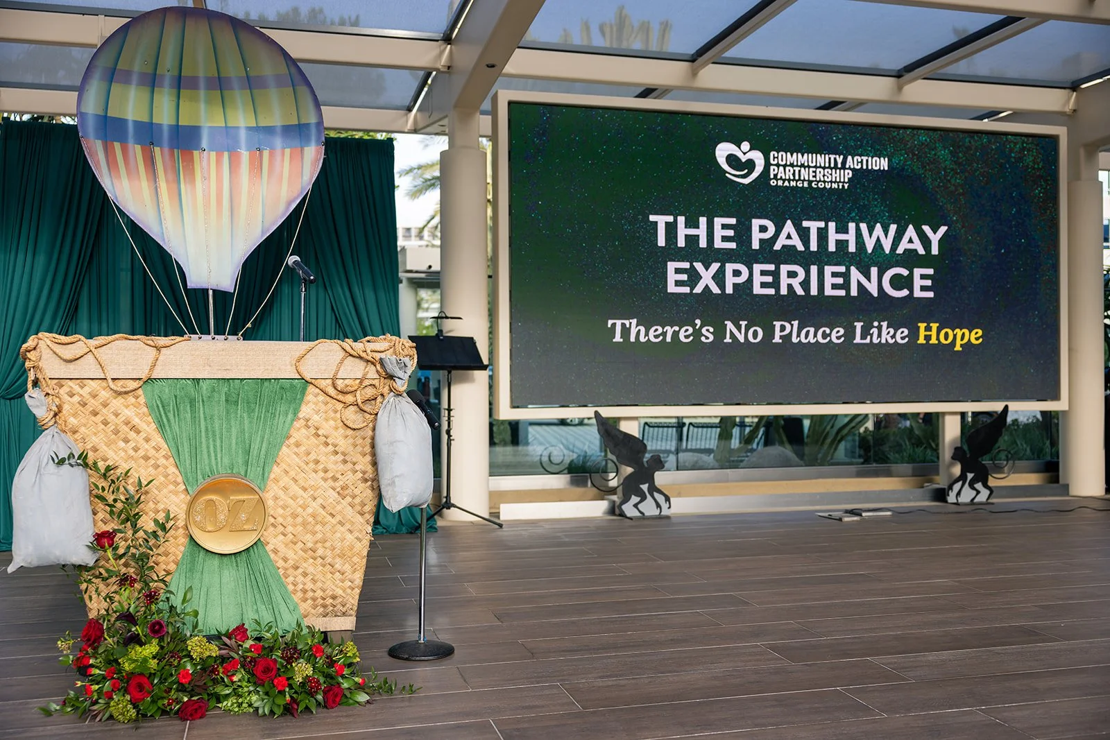 An indoor stage setup with a hot air balloon-shaped prop, a basket decorated with green fabric and flowers, and a large screen displaying 'The Pathway Experience - There's No Place Like Hope'.