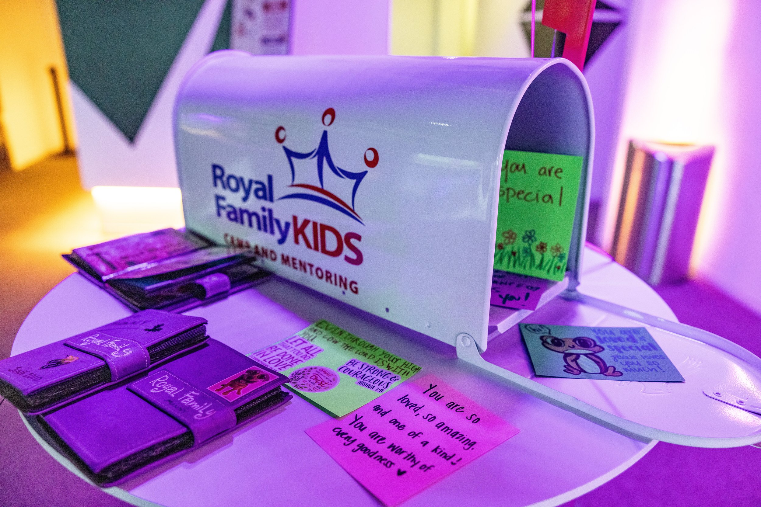 A donation box with the Royal Family Kids logo and various motivational messages and flyers about kids and families on a table.