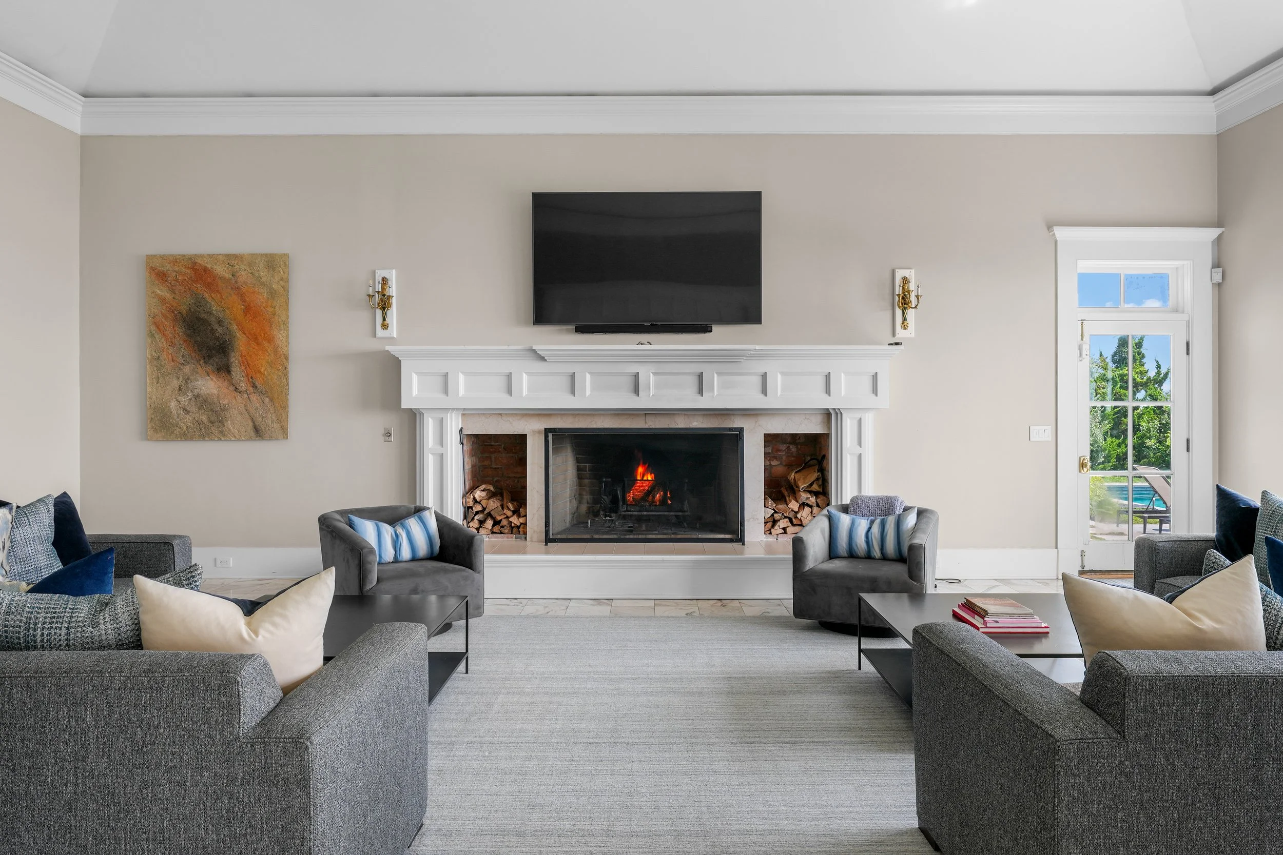 Living room with a fireplace, wall-mounted TV, modern sofas and armchairs, a painting, and a doorway with a view outside.