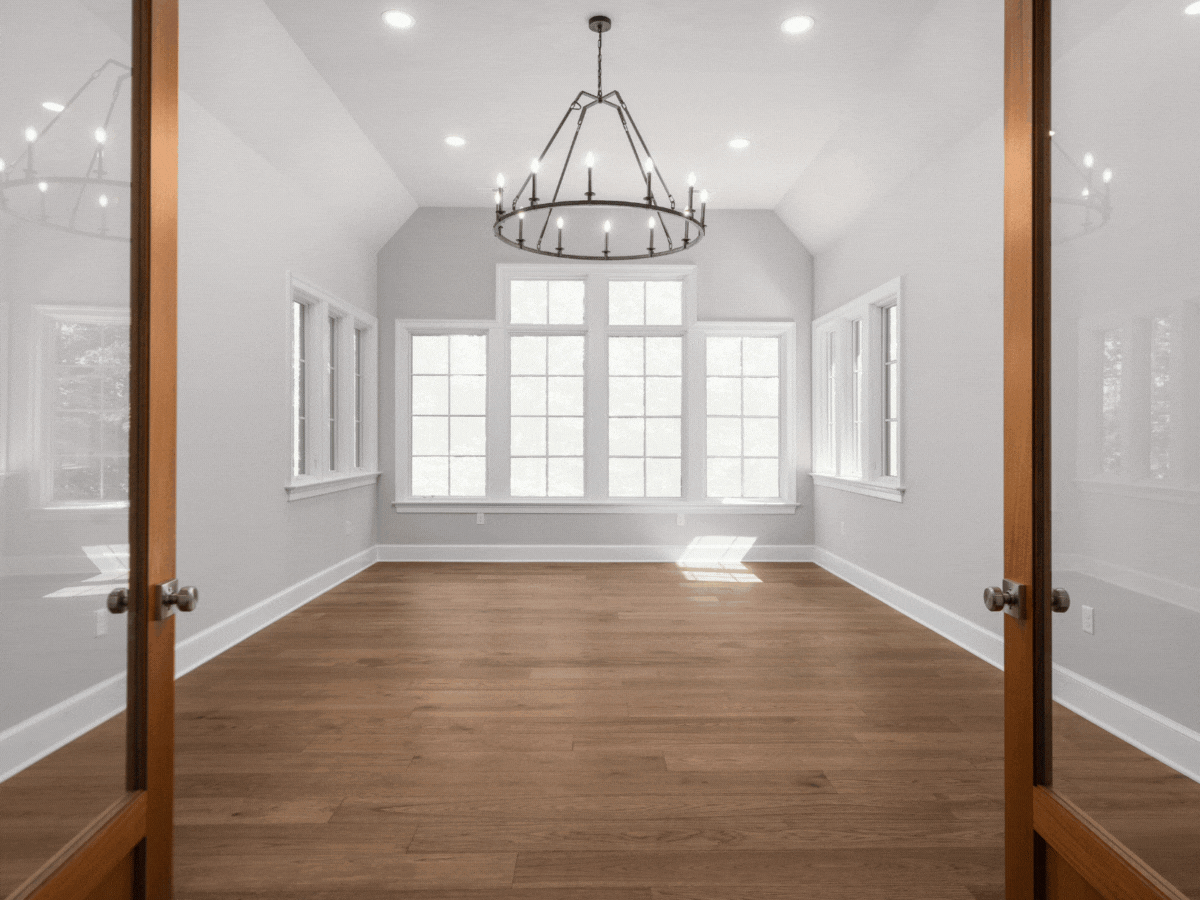 Empty dining room with large windows, wooden floors, white walls, and a black chandelier.