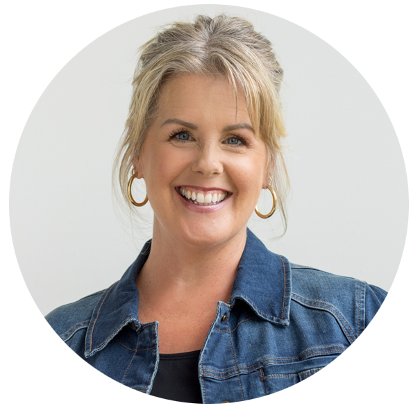 Smiling woman with blonde hair and blue eyes, wearing a denim jacket and gold hoop earrings, posing in front of a white background.