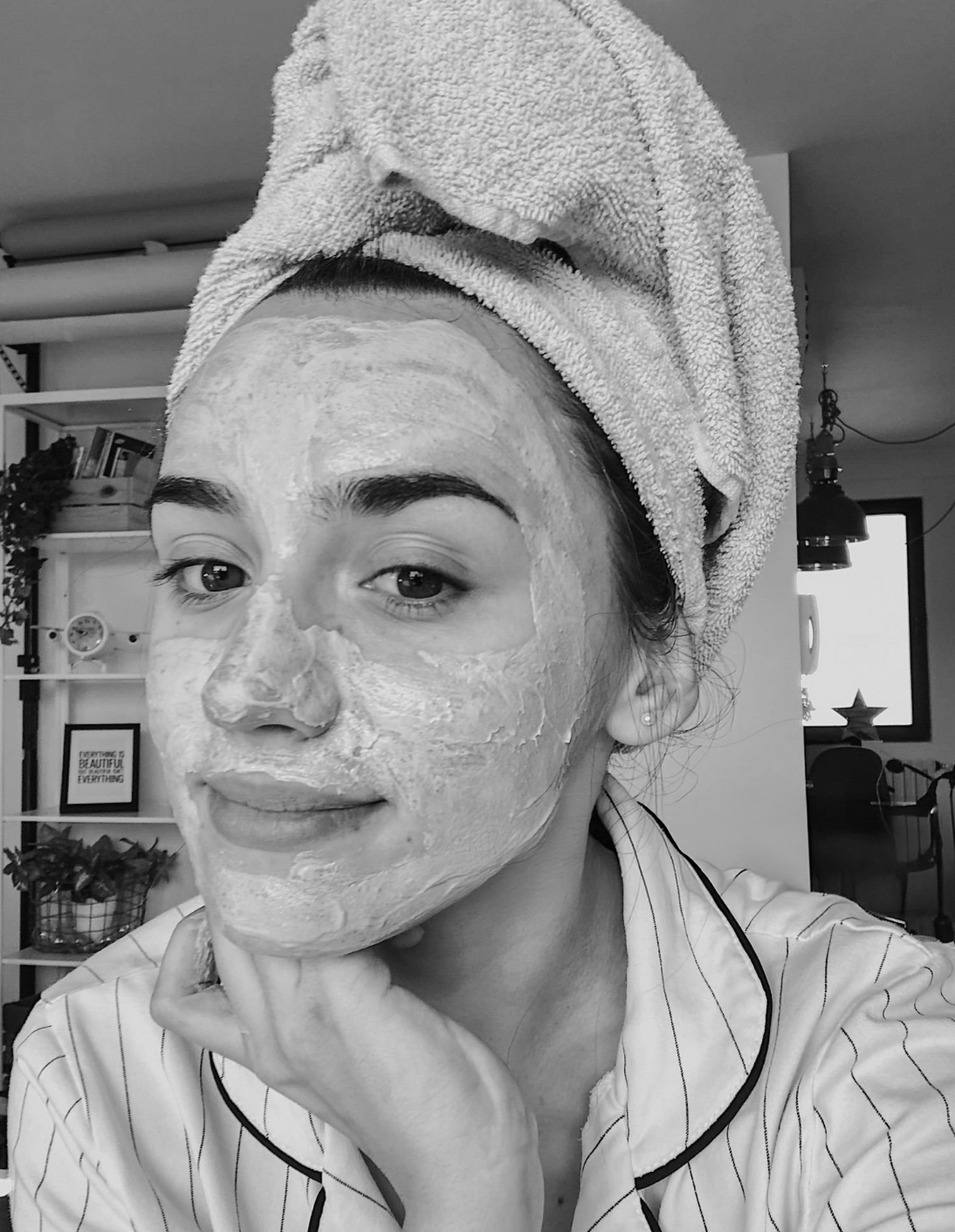 Black and White image of influencer with hair in a towel and face mask on.