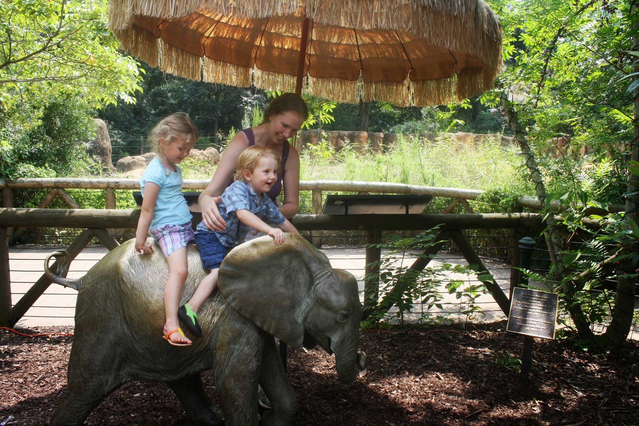 Mother and two young children laughing together at a zoo exhibit, representing the family-centered care and real-life experiences supported by Play to Say Therapy