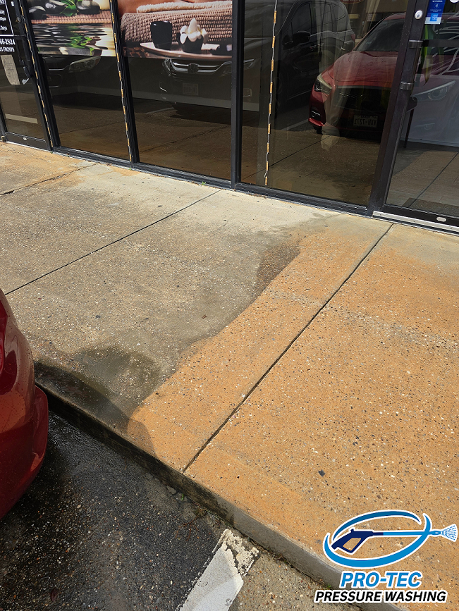 Sidewalk with uneven concrete sections and water pooling near a glass storefront, reflecting indoor furniture and cars outside.