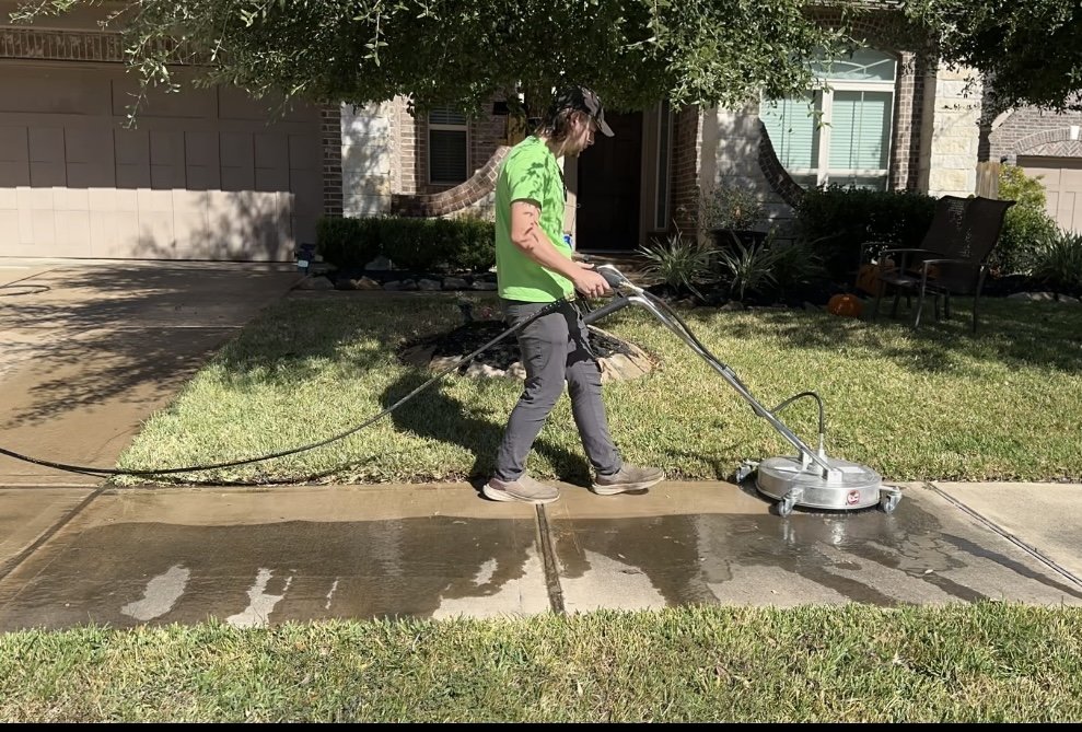 Person using a power washer to clean the sidewalk in front of a house.