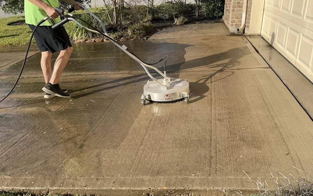 Person using a power washer to clean a concrete driveway at sunset.