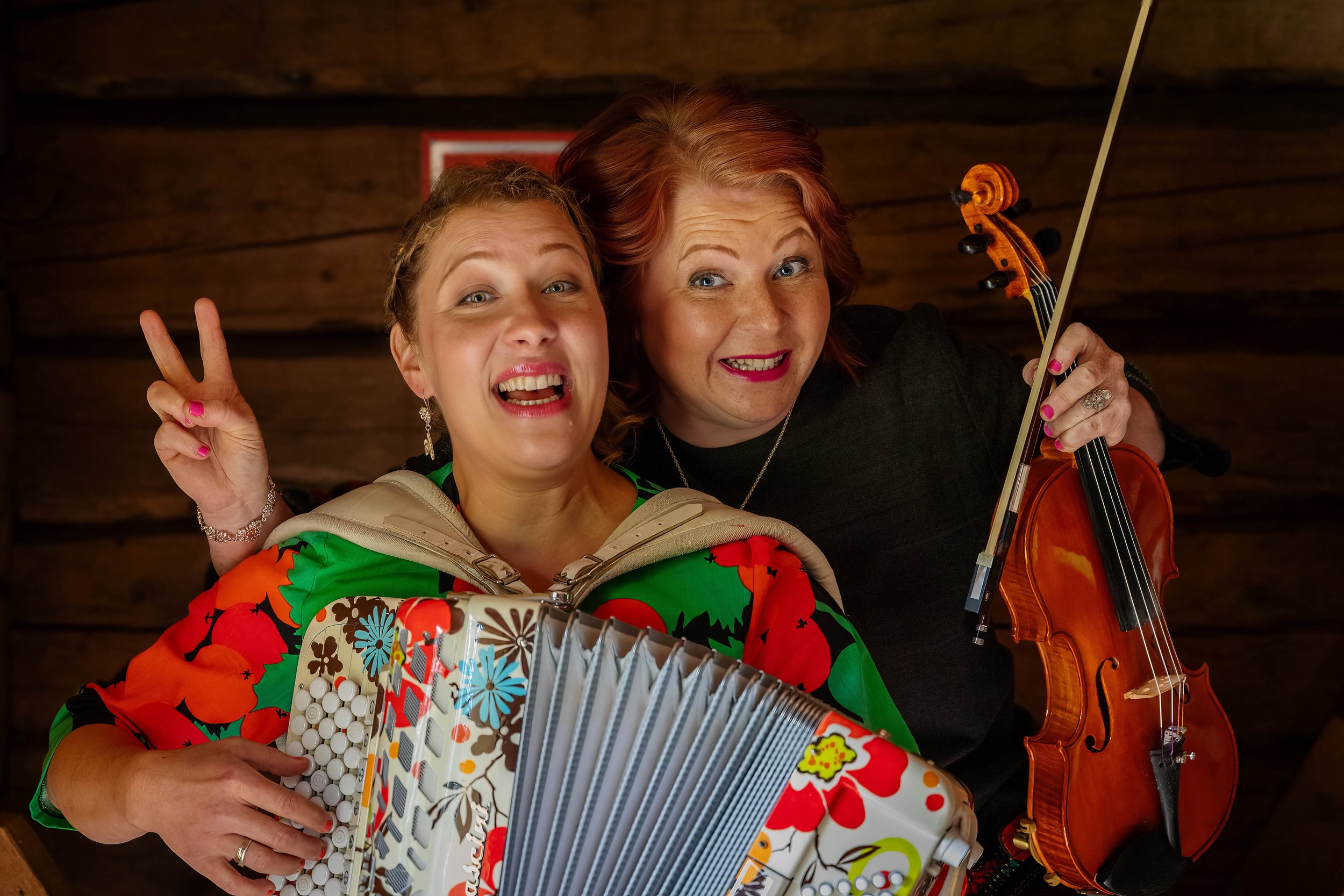 Petra ja Riitta esiintyvät iloisina ja hymyilevinä viulu- ja haitarimusiikin parissa. Kuva välittää energisen, positiivisen ja musiikista nauttivan tunnelman.