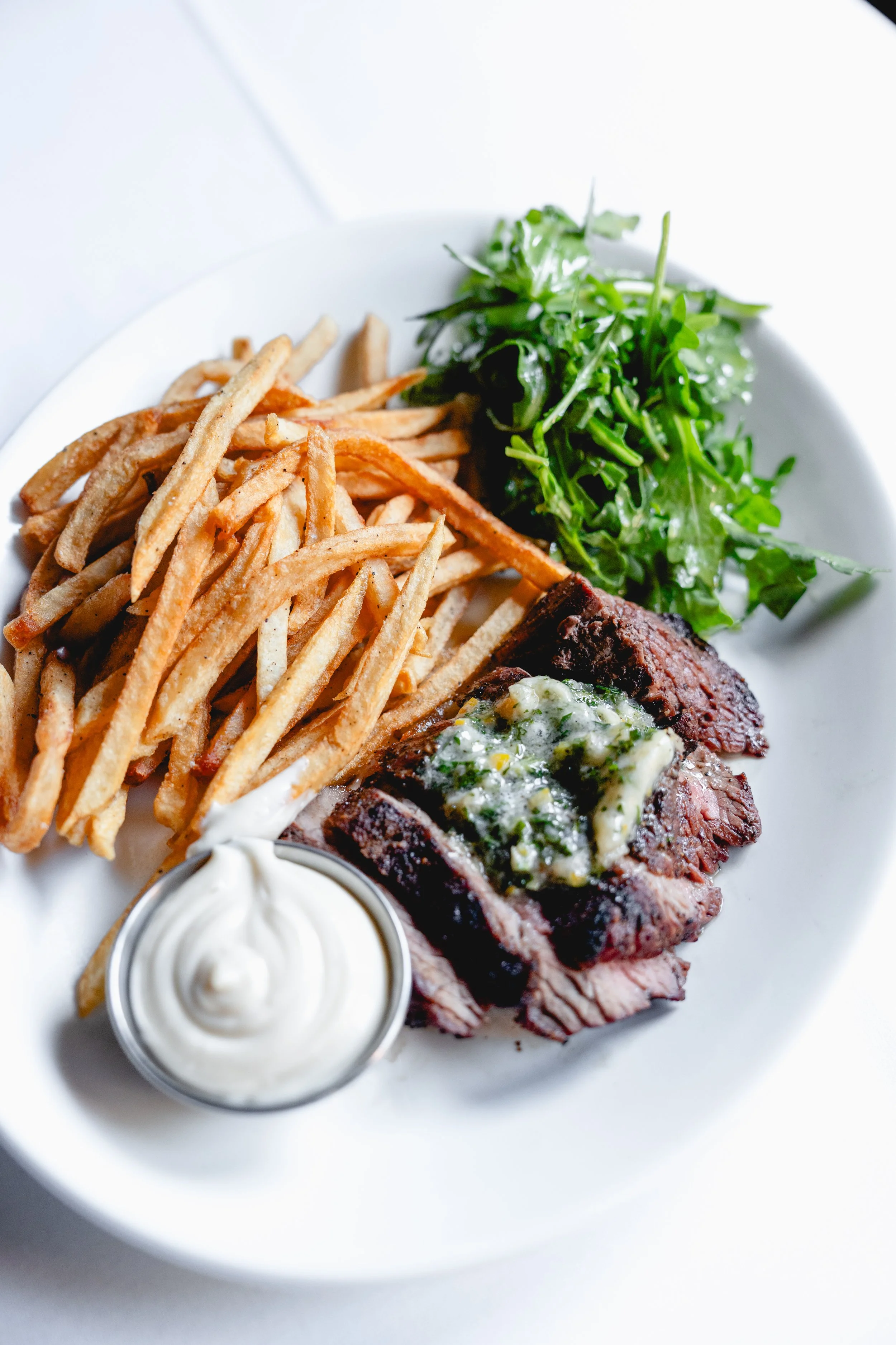 Featured entree of Steak Frites served with Sauce Au Poivre, Tallow Fries, Petit Salad.