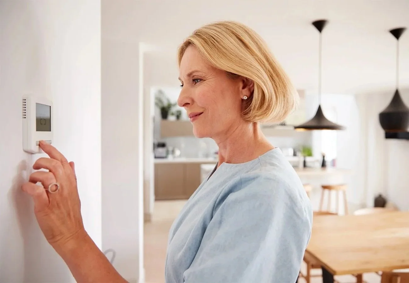 Older woman adjusting a thermostat after local Redding HVAC contractor working on air conditioning system