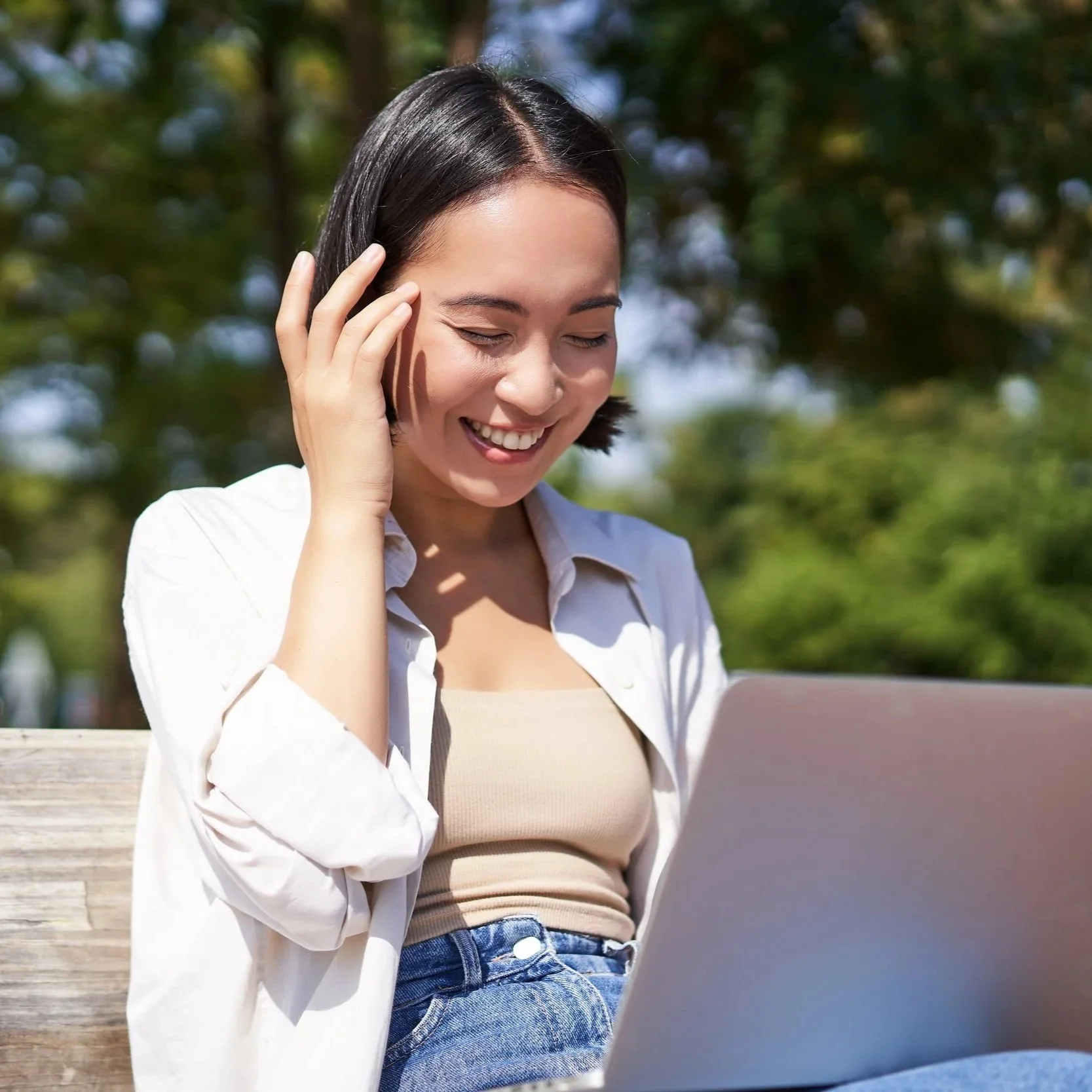 Woman laughing while using a laptop on a park bench