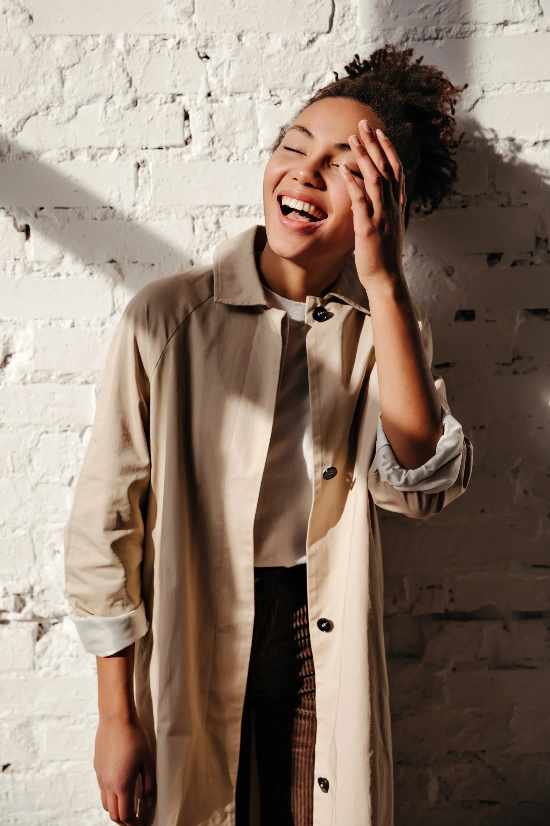 Stylish woman laughing indoors while wearing a trench coat