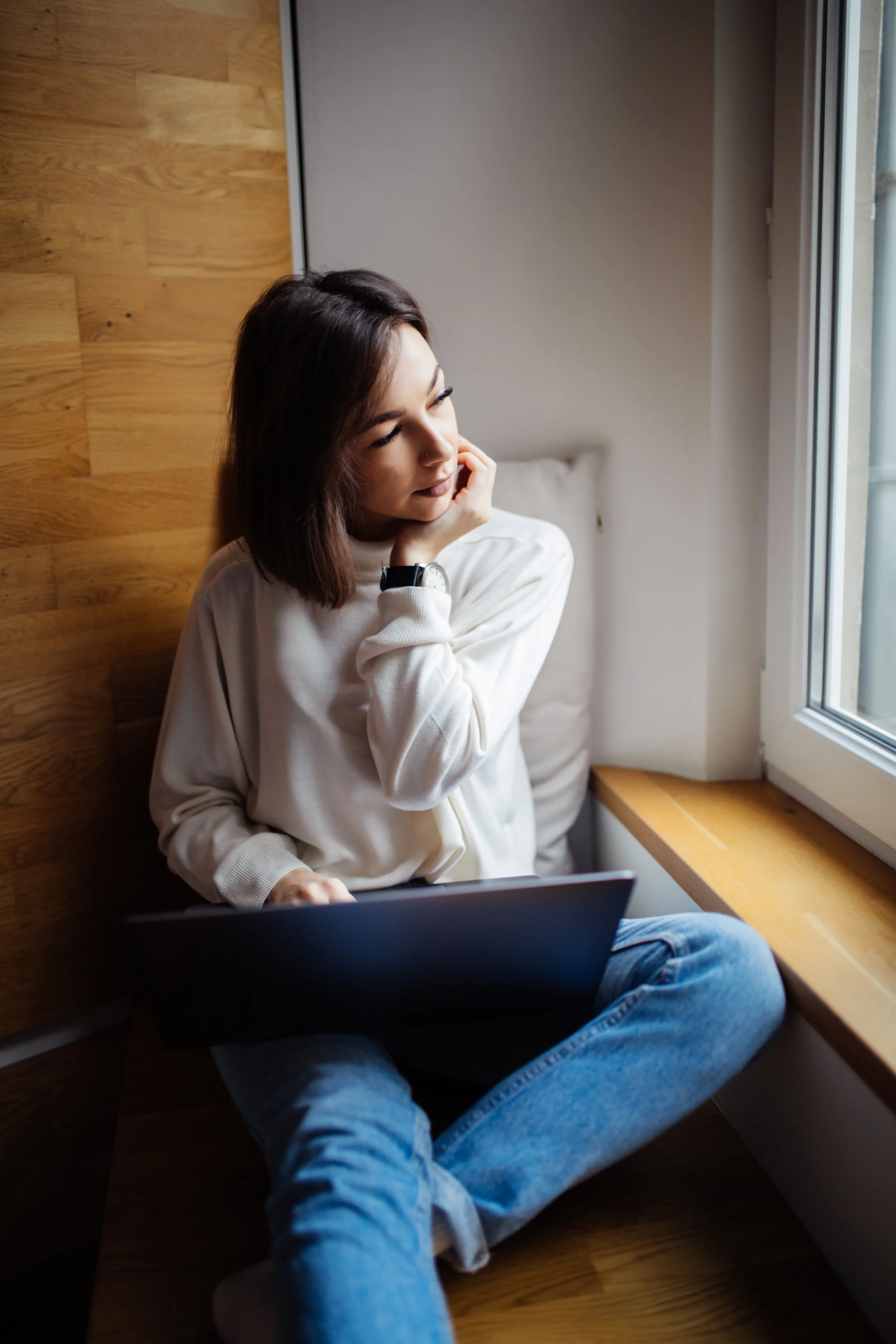 Woman sitting on a windowsill while working on a laptop