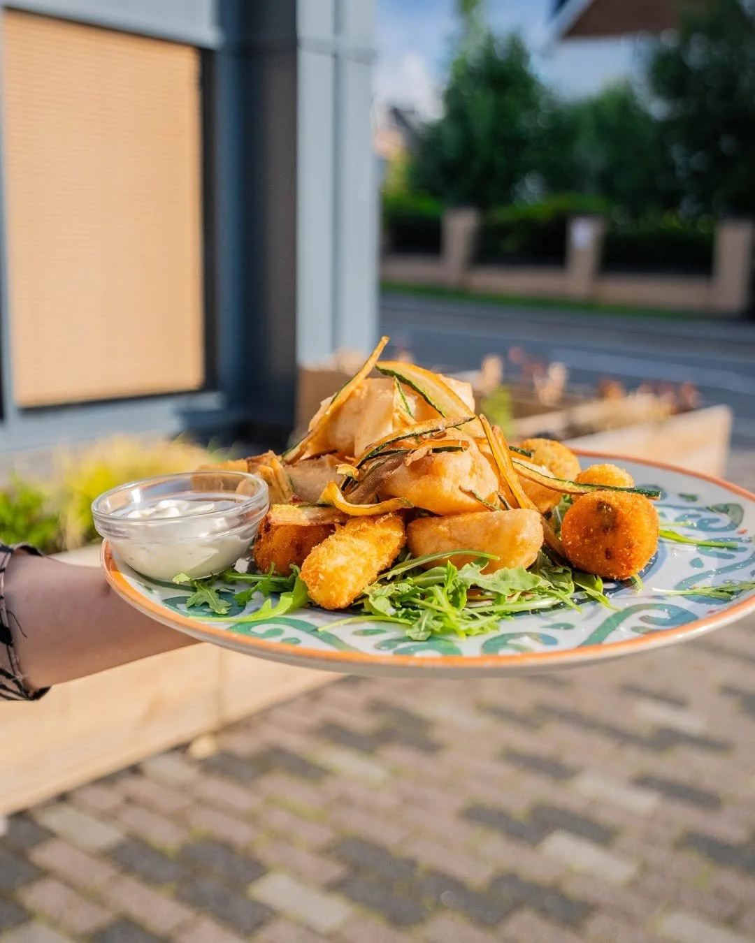 Plate of fried food with dipping sauce on a decorative plate, held outdoors with a blurred street background.