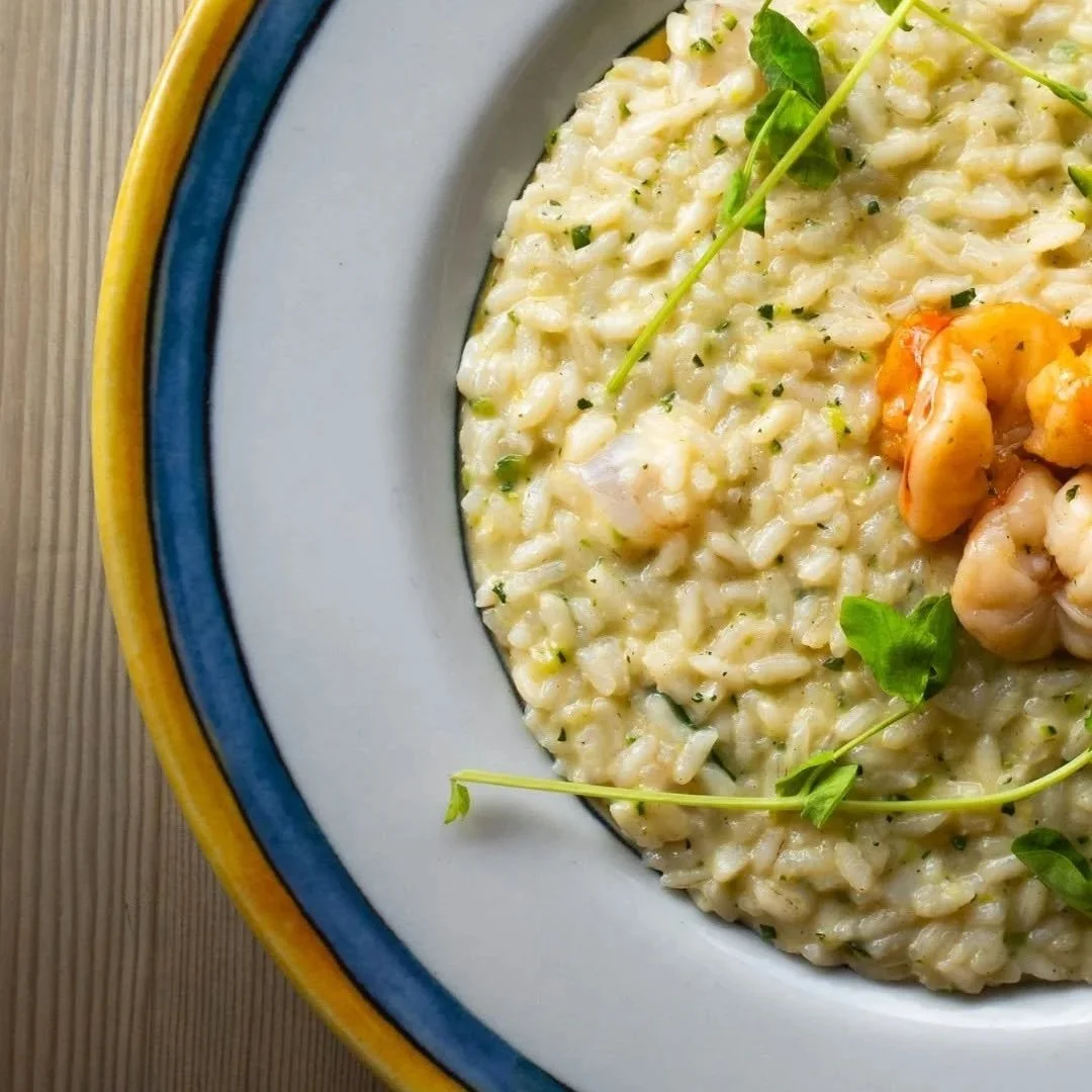 Creamy risotto with small pieces of shrimp and garnished with microgreens on a colorful border plate.