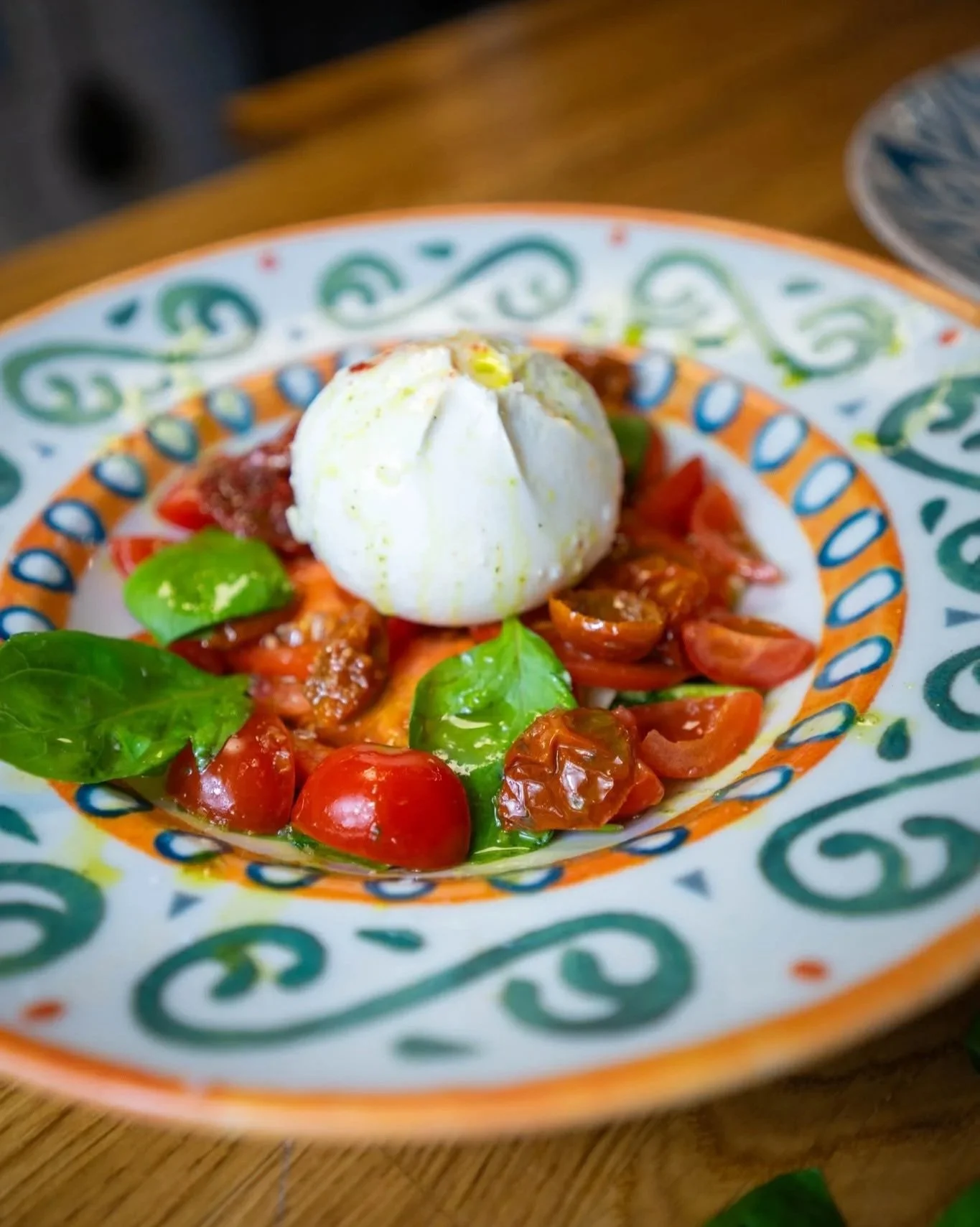 Caprese salad with cherry tomatoes, basil leaves, mozzarella ball, and balsamic glaze on a decorative plate. PepeNero Pizza Restaurant