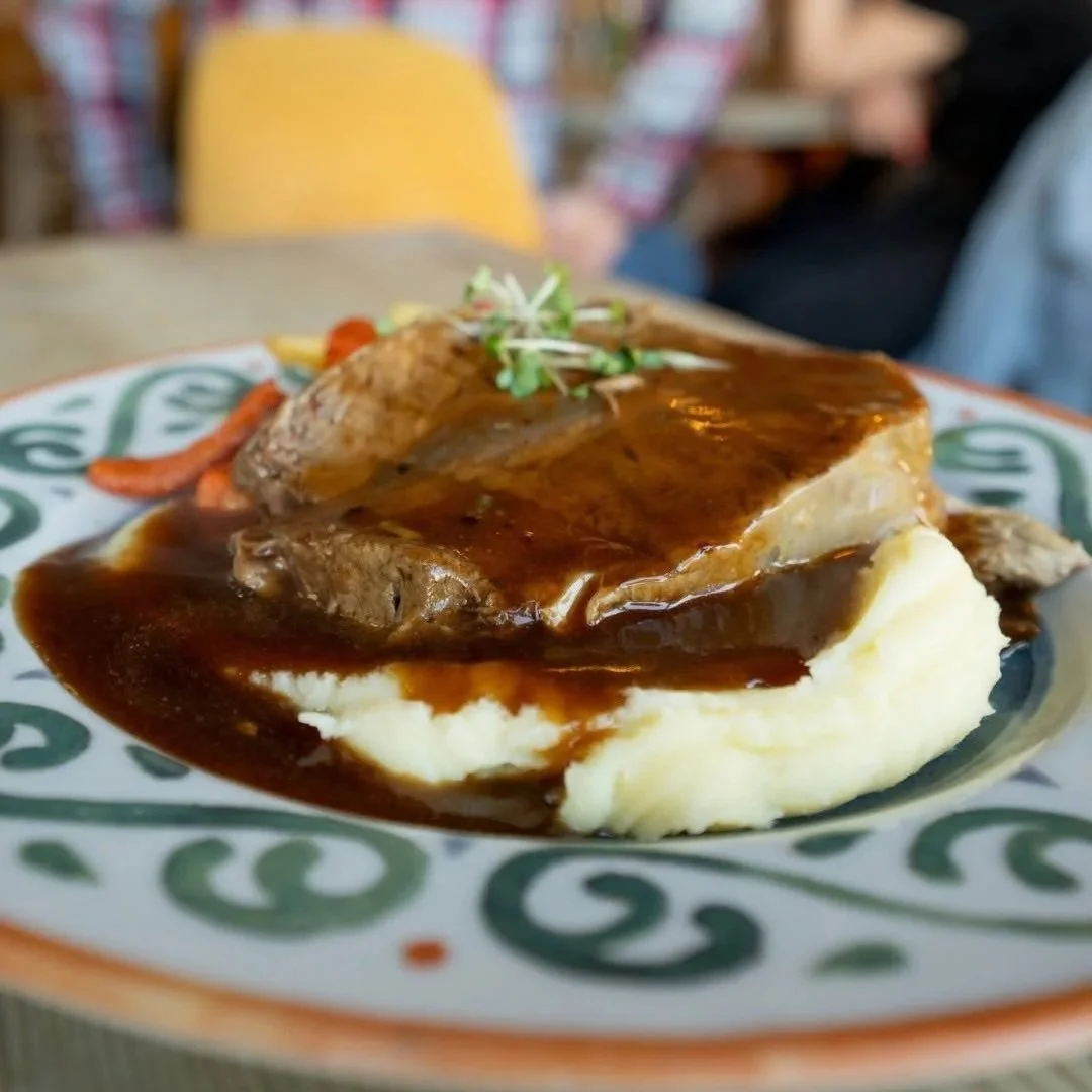 Plate of mashed potatoes topped with beef stew and gravy, garnished with microgreens.