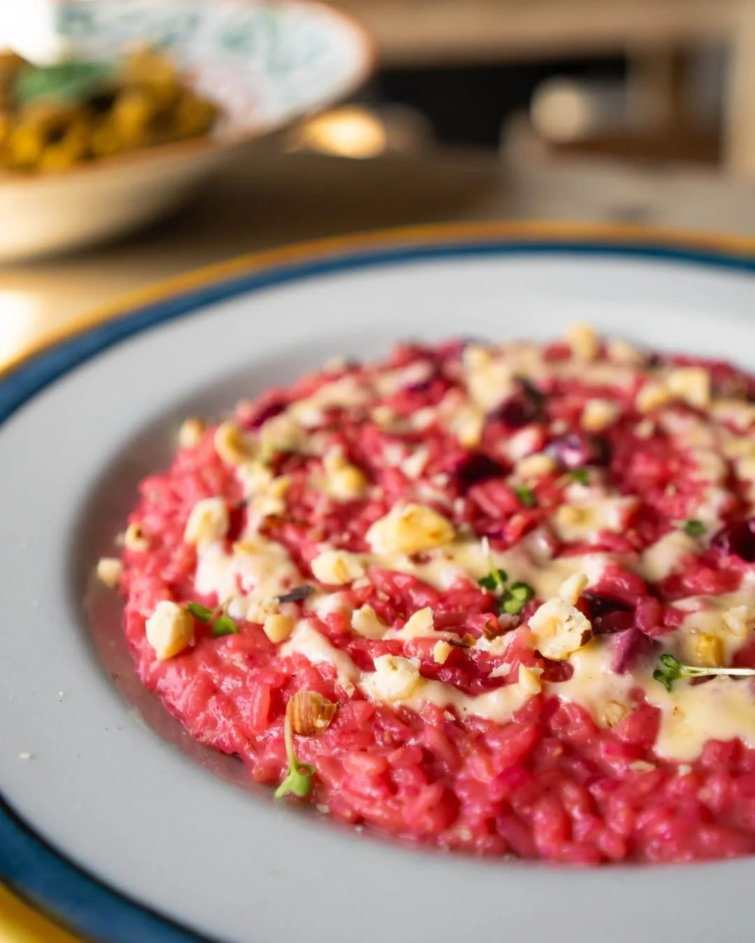 Close-up of a plate of beetroot risotto topped with chopped nuts and herbs. PepeNero Pizza Restaurant