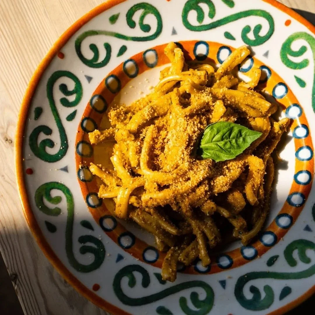 Plate of pasta with a basil leaf, sprinkled with cheese, in a decorative dish with green, orange, and blue patterns.