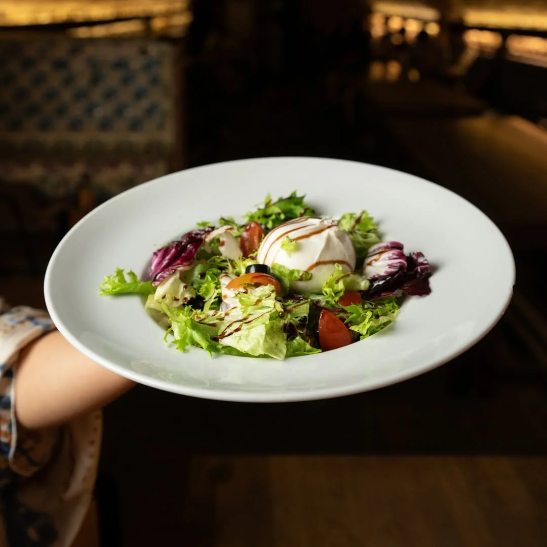 Fresh garden salad with mixed greens, cherry tomatoes, a scoop of mozzarella cheese, and a drizzle of balsamic glaze, on a white plate. PepeNero Pizza Restaurant