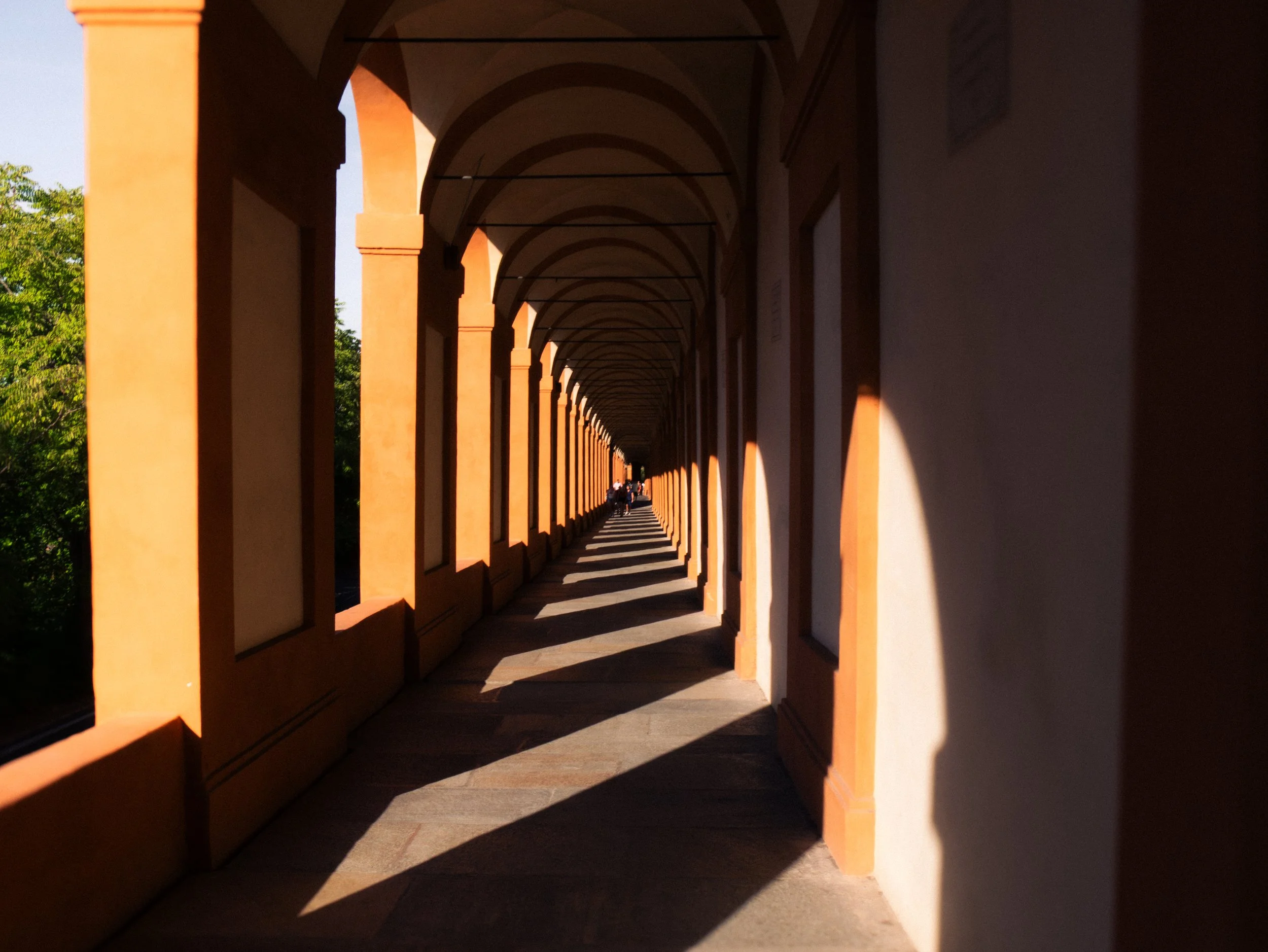 Long corridor with arched ceiling and orange columns, sunlight creating shadow patterns on the floor.