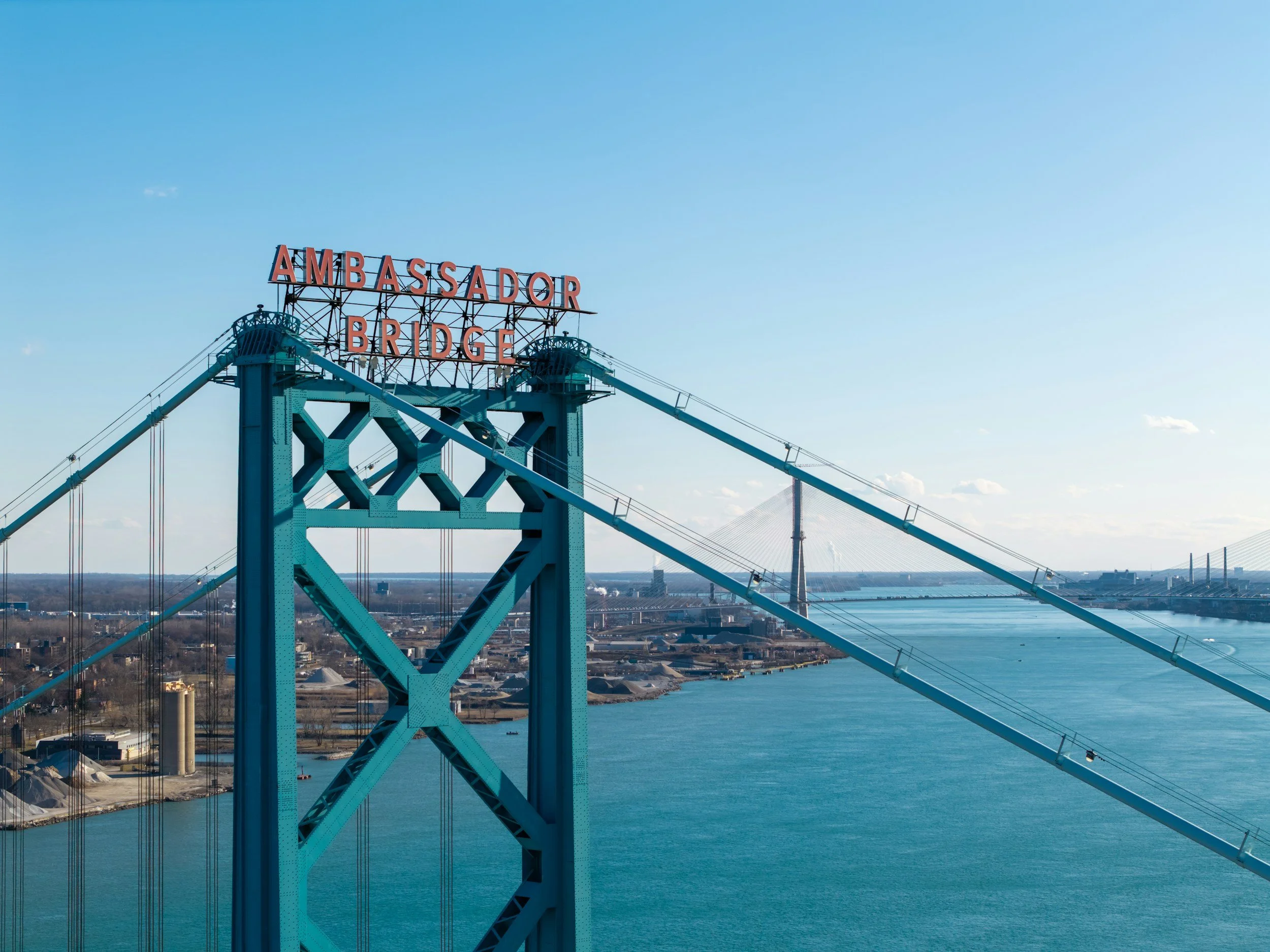 View of the Ambassador Bridge with suspension cables over the Detroit River and the Detroit skyline in the background on a clear day.