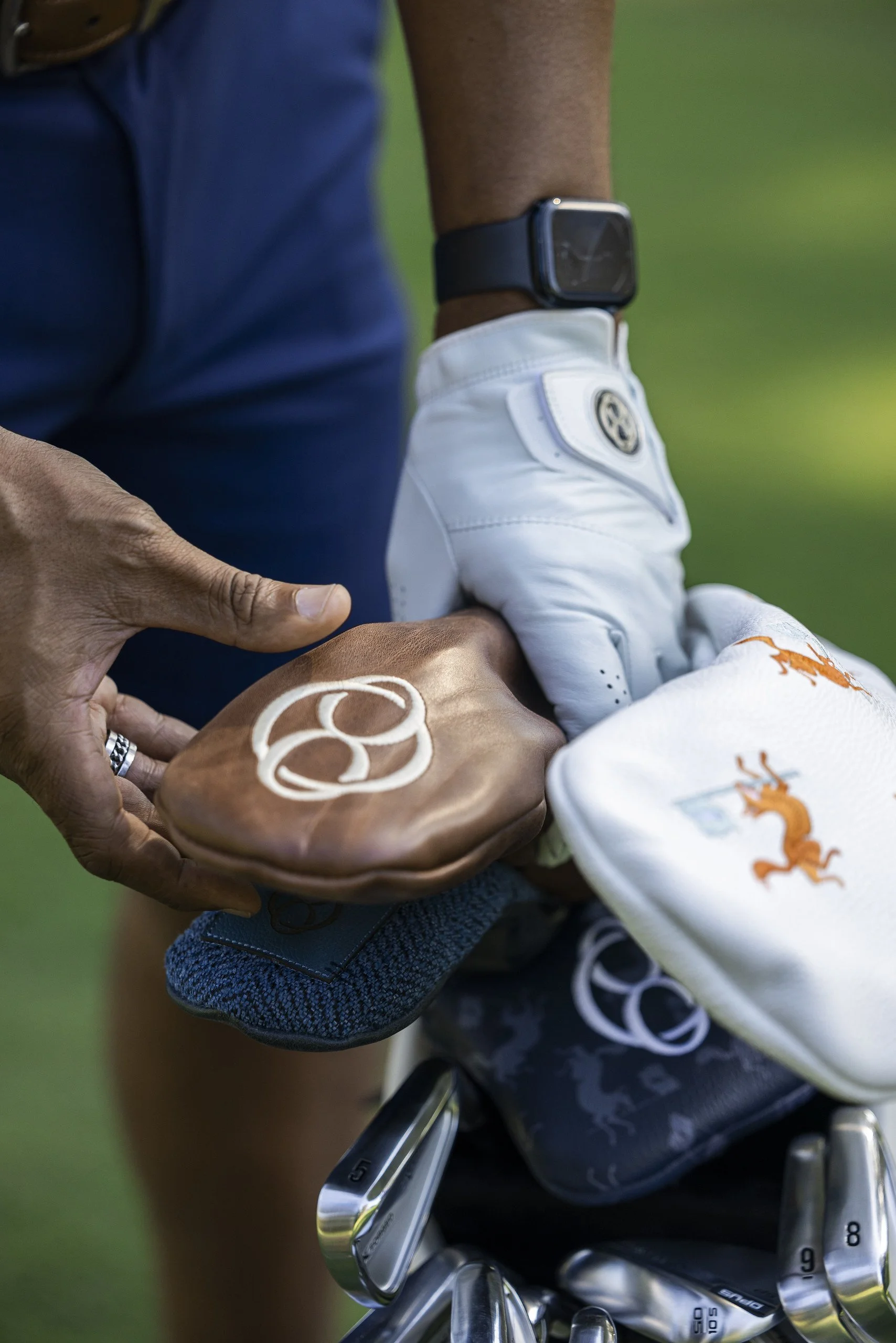 Person placing a baseball glove in a golf club bag on a golf course.