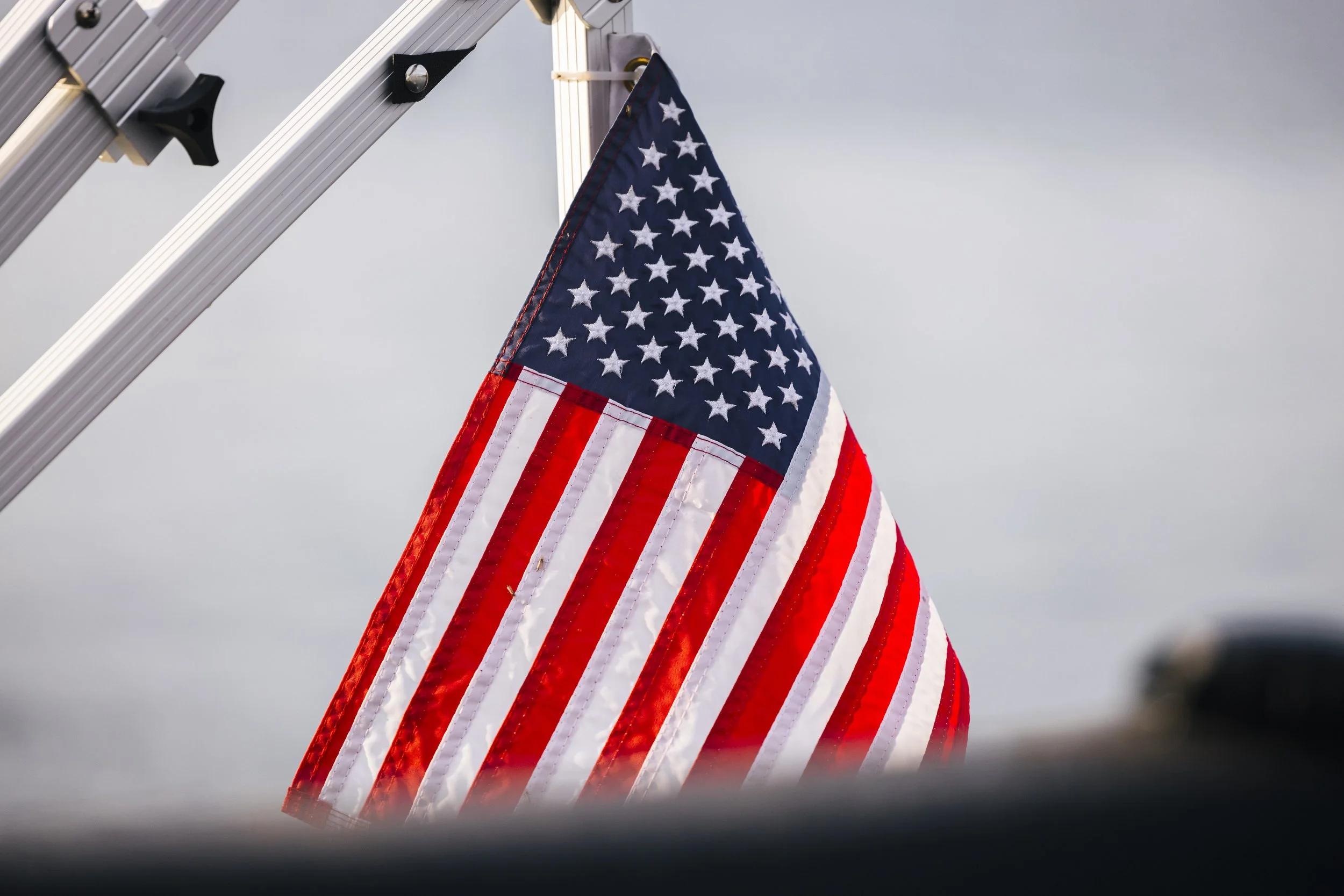 An American flag hanging from a metal pole against a gray sky.