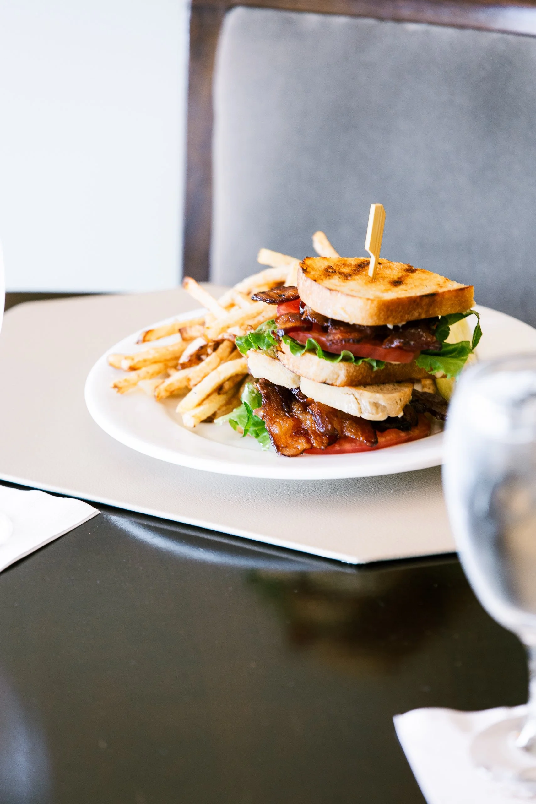 A plate with a stacked club sandwich and a side of French fries on a table.