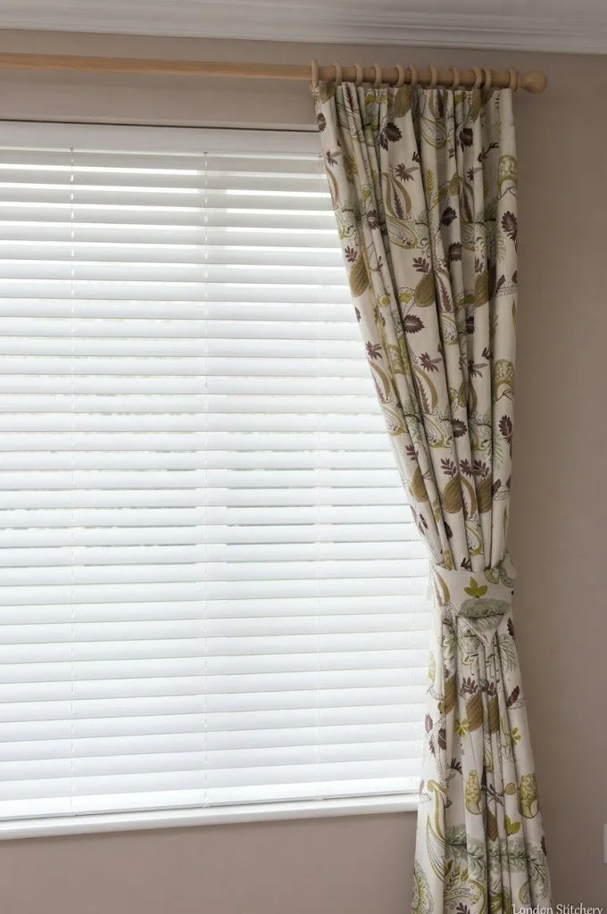 Custom floral patterned single drapery panel with a tie-back, elegantly framing a bright white window blind by London Stitchery.