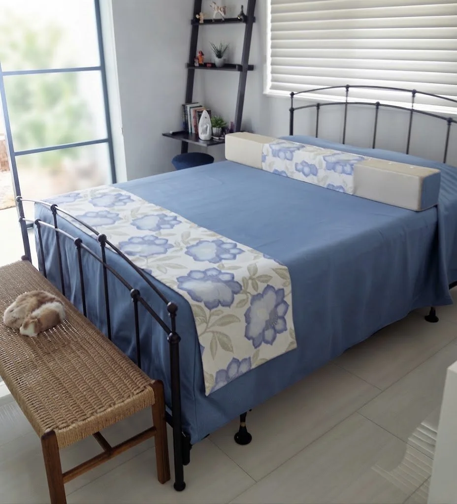 Custom blue quilted coverlet set paired with tailored bolster pillows and a coordinating floral runner, showcasing bespoke craftsmanship for a refined bedroom design.