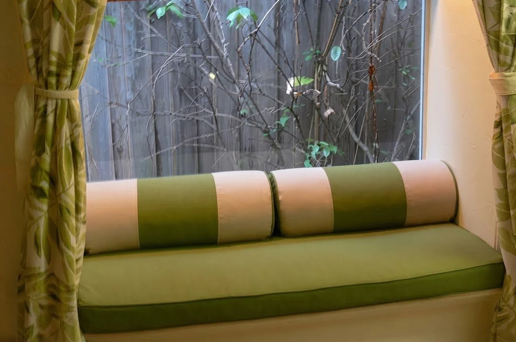 A custom green window seat cushion paired with matching cylindrical half-bolster pillows, tailored by London Stitchery.