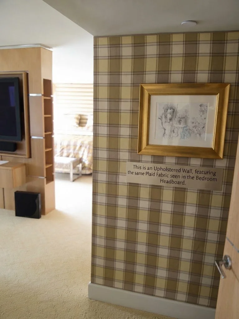 Custom upholstered accent wall paired with bespoke coordinated plaid wall paneling, creating a seamless, high-end texture for a sophisticated bedroom suite.