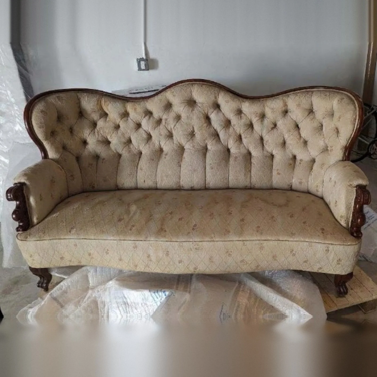 Antique 1870s Victorian sofa before restoration, with worn cream tufted fabric and a carved wooden frame.