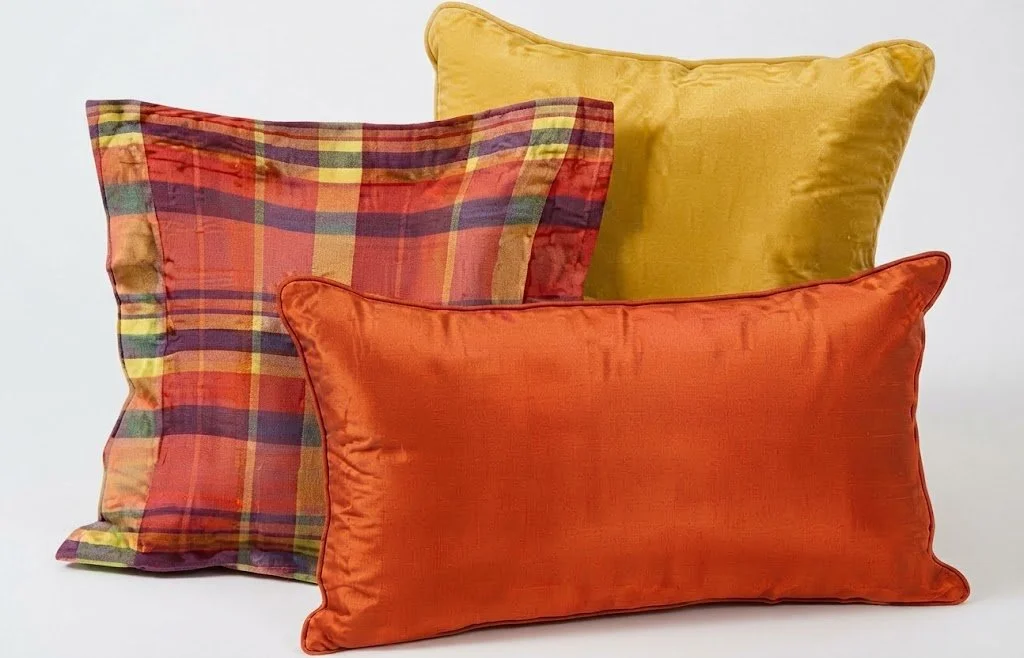 A stack of luxury designer pillows featuring vibrant citrus-toned silk and plaid fabrics with knife-edge tailoring, custom-crafted by London Stitchery.